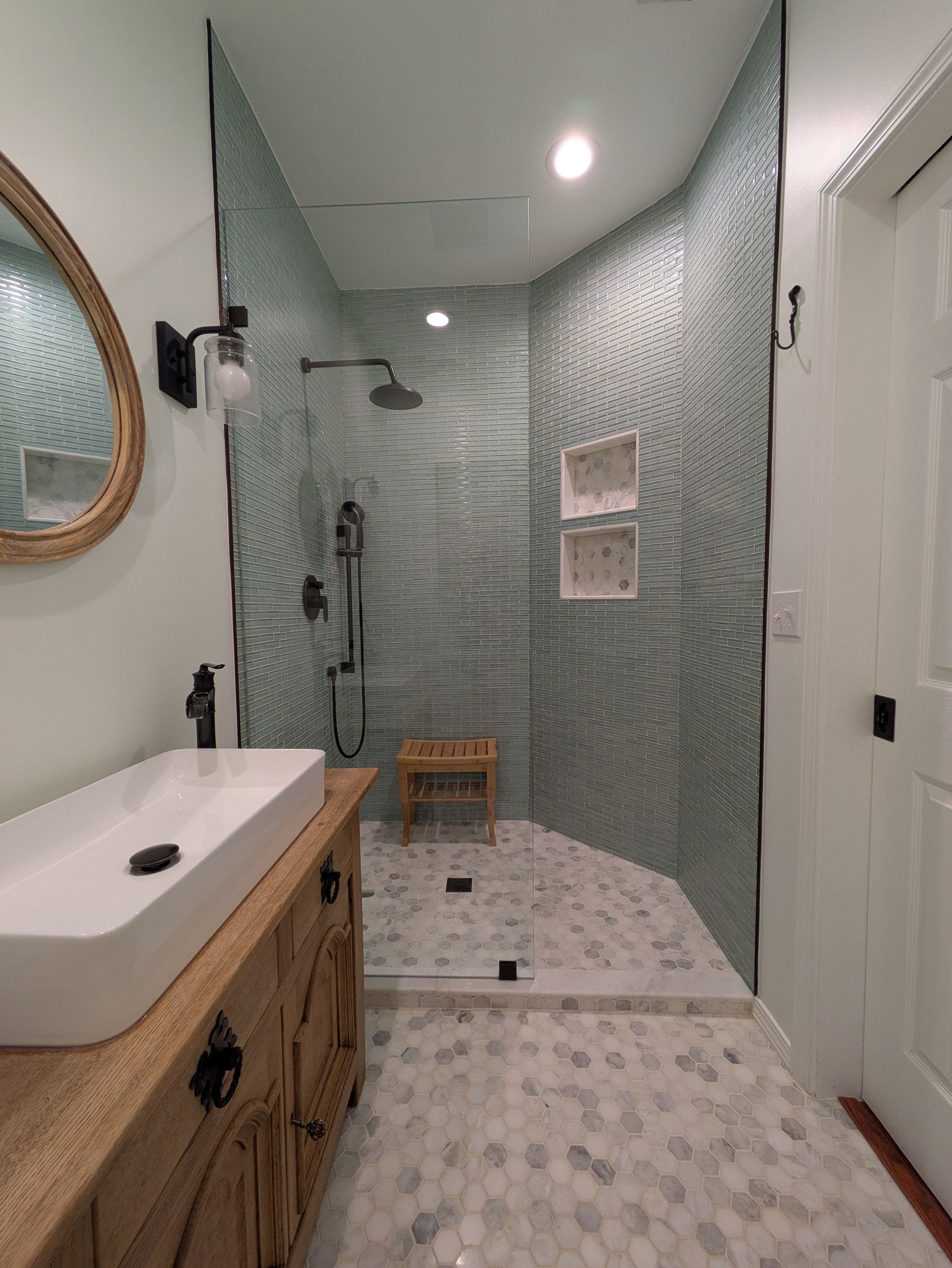 Bathroom with light blue tiled shower, glass door, and white vanity with a rectangular sink.
