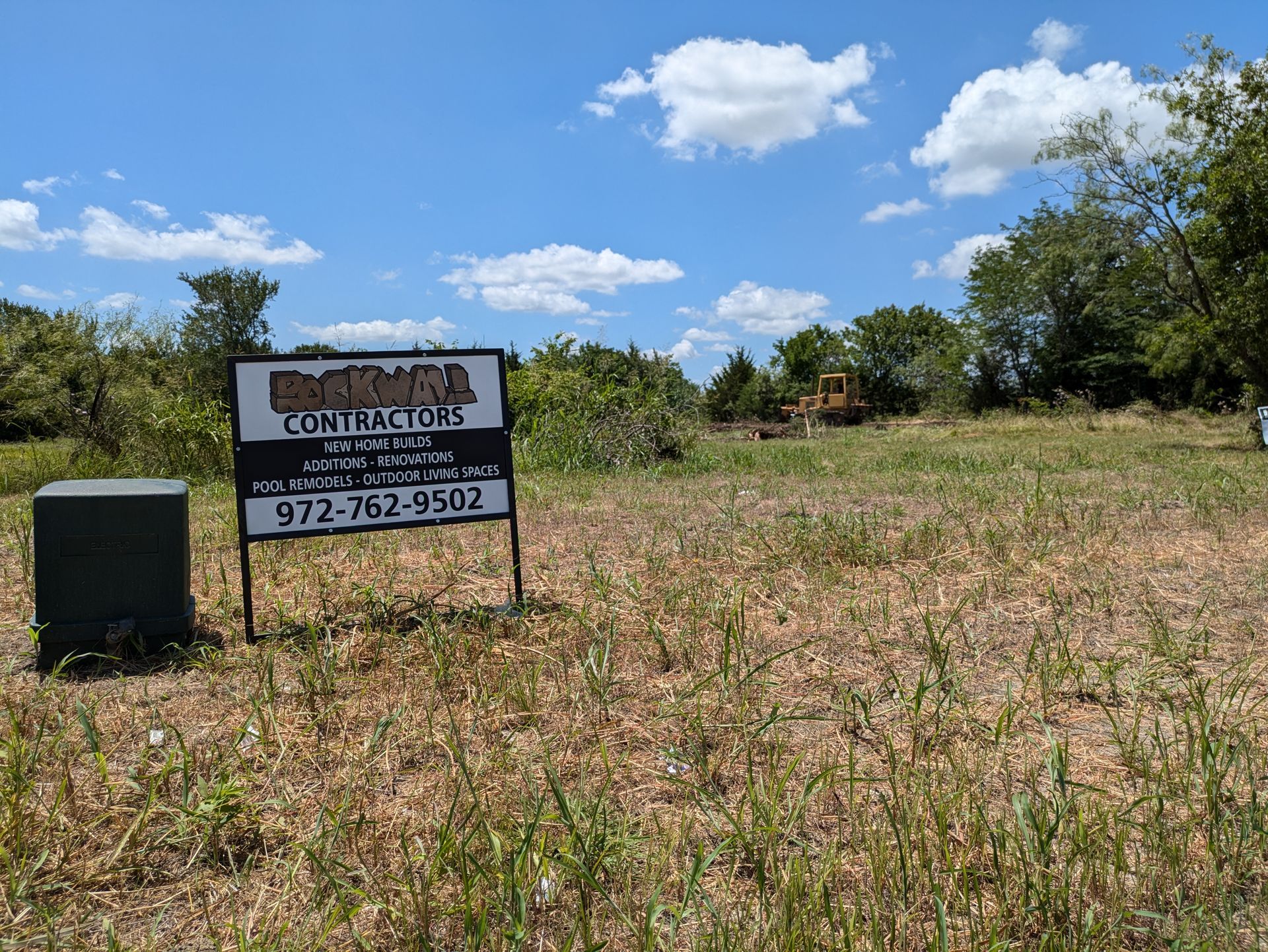 Sign for construction contractors at a vacant lot; bulldozer in the background.
