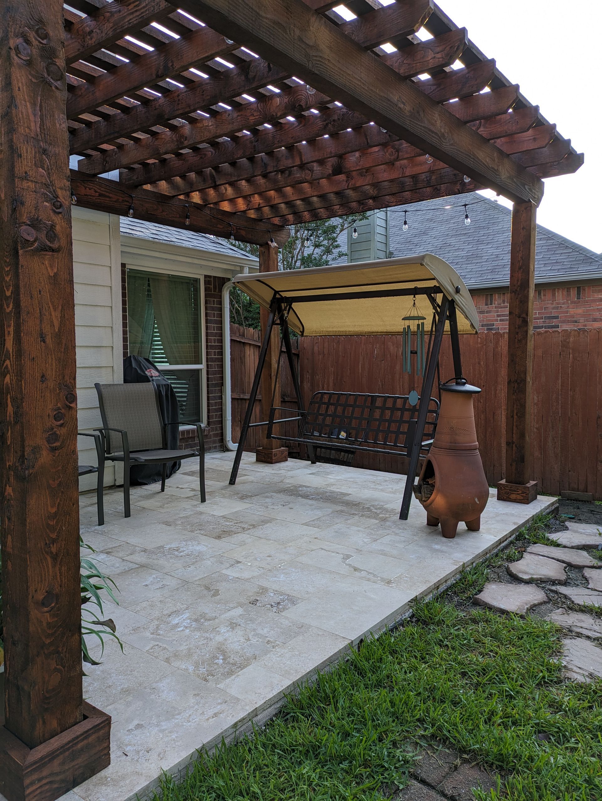 There is a swing under a pergola in the backyard.