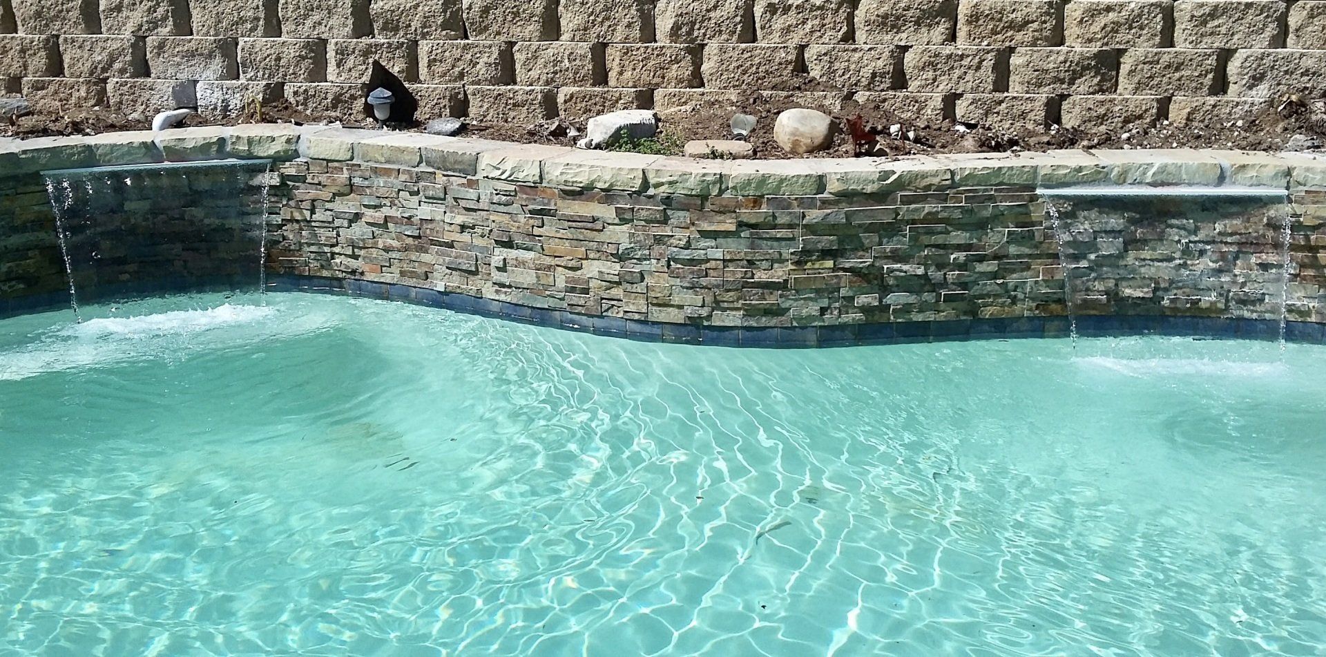 A swimming pool with a stone wall and a waterfall