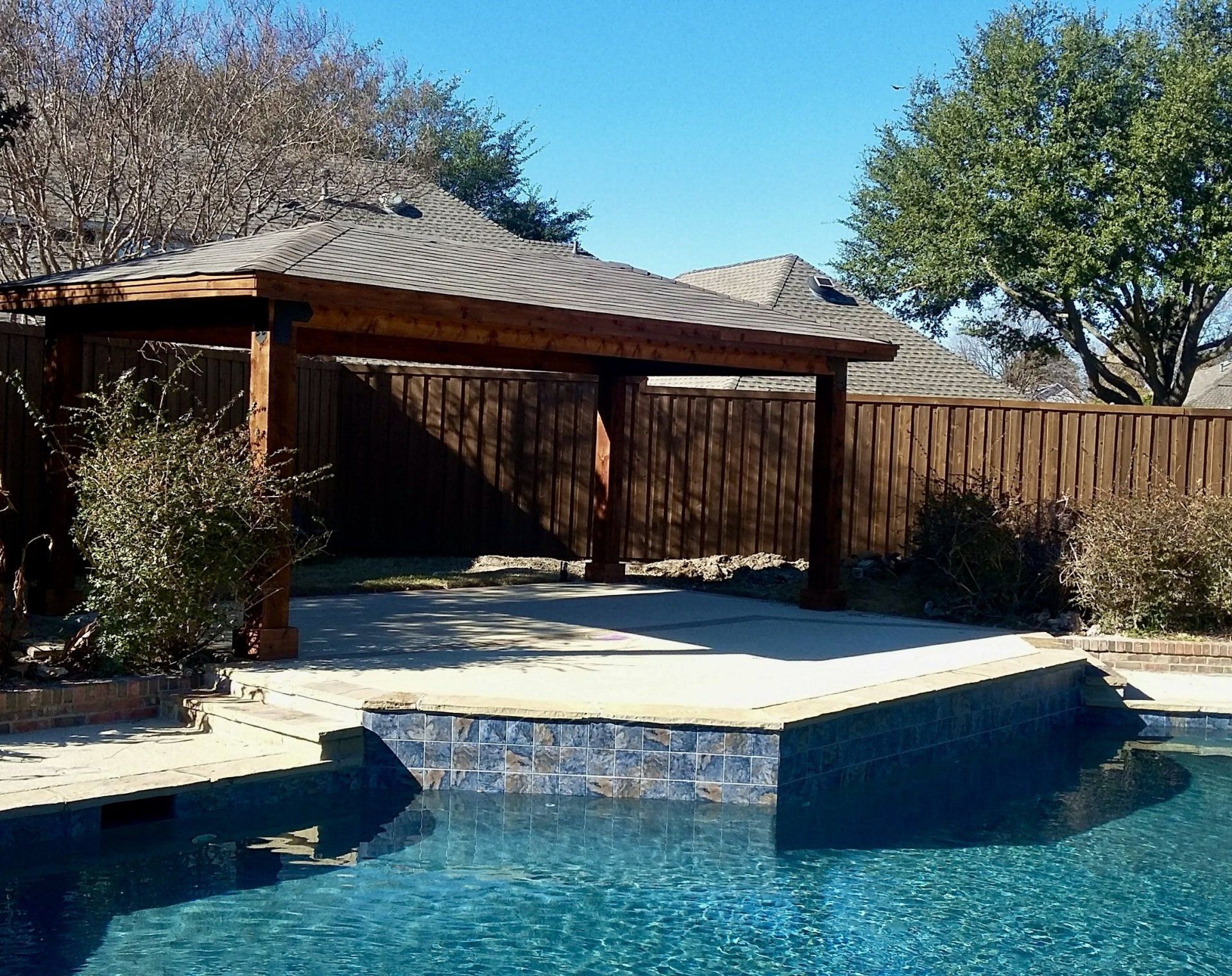 A swimming pool with a wooden gazebo in the background