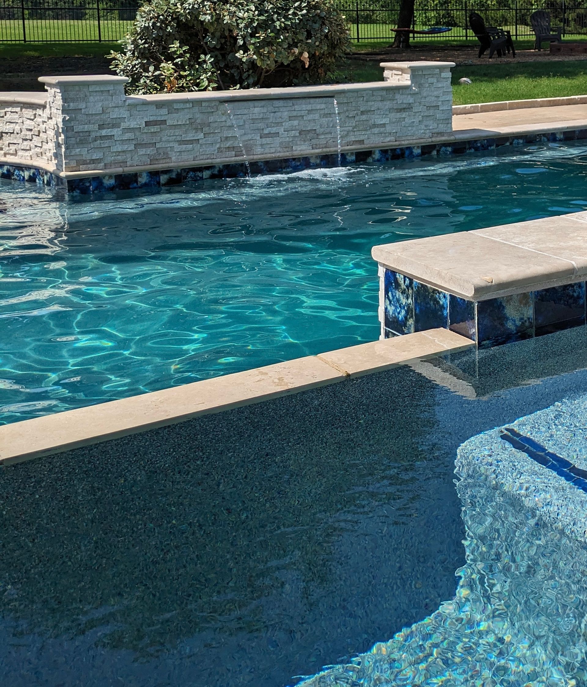A large swimming pool with blue tiles and a stone wall surrounding it.