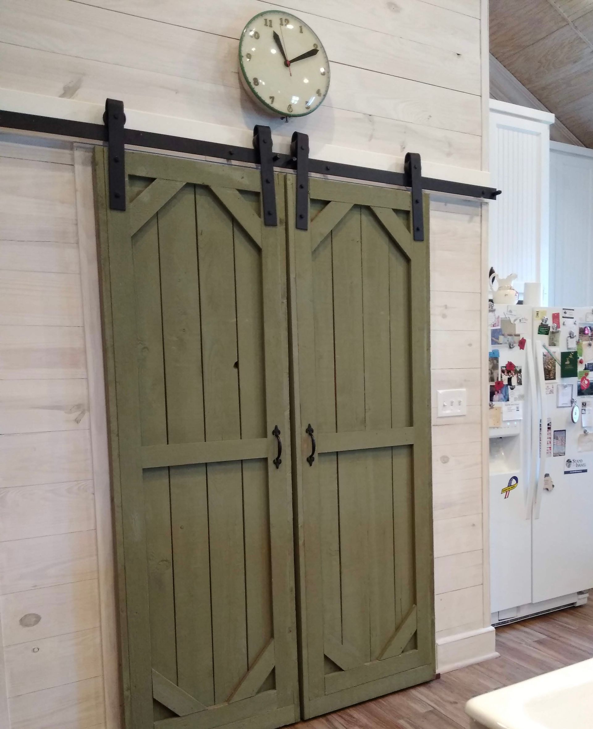 A clock hangs above a pair of green sliding barn doors