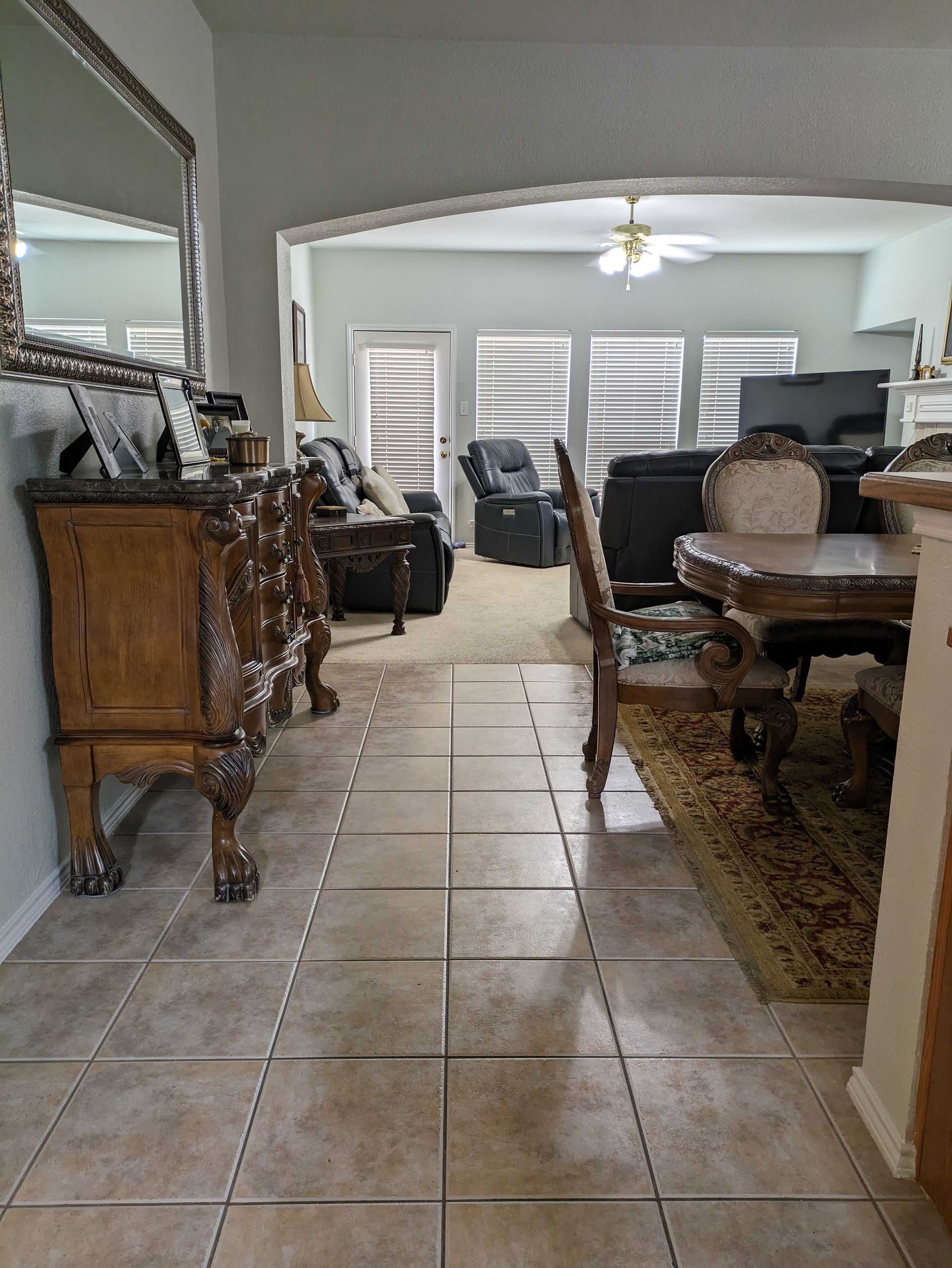 Entryway with ornate furniture, beige tile floor, and view into living room with seating and windows.