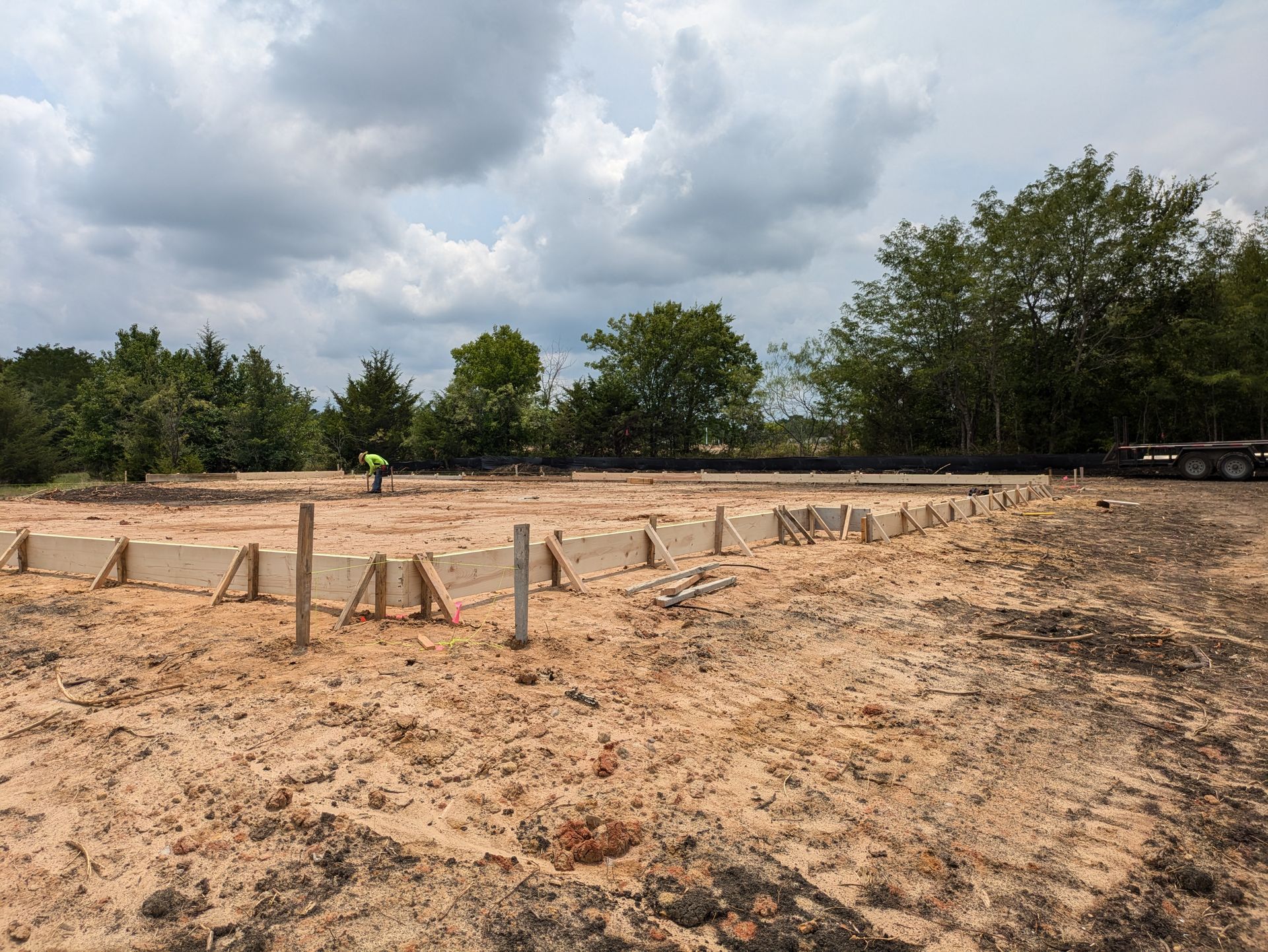 Construction site with concrete forms set on dirt; a person in the distance is working.