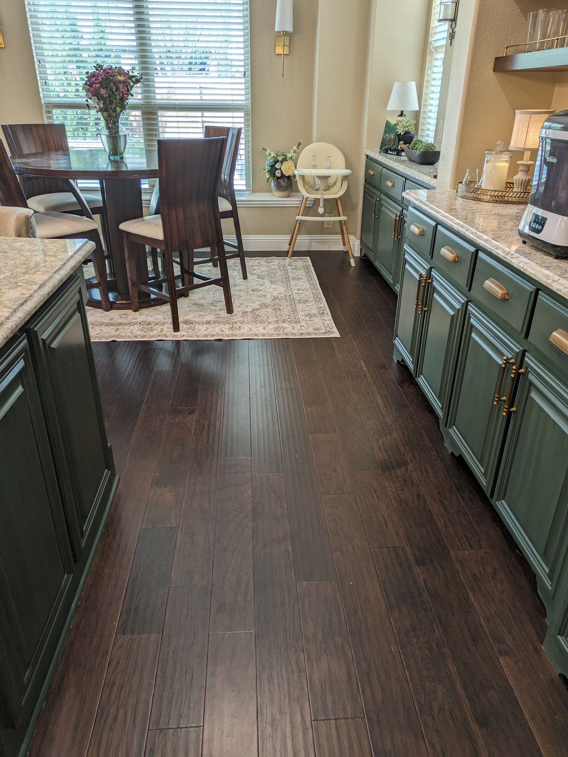 A kitchen with wooden floors , green cabinets , a table and chairs.
