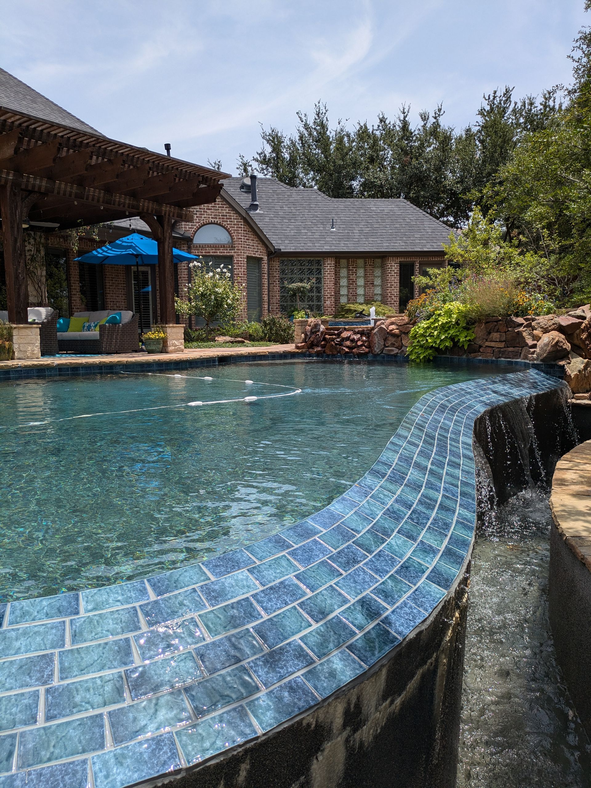 A large swimming pool with a waterfall and a house in the background.