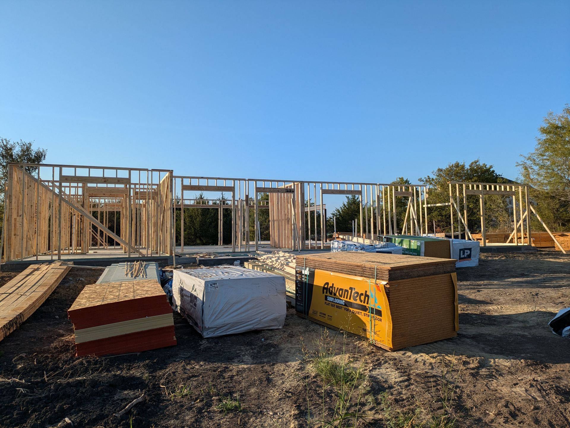 Wooden frame of a house under construction; materials and clear sky in background.