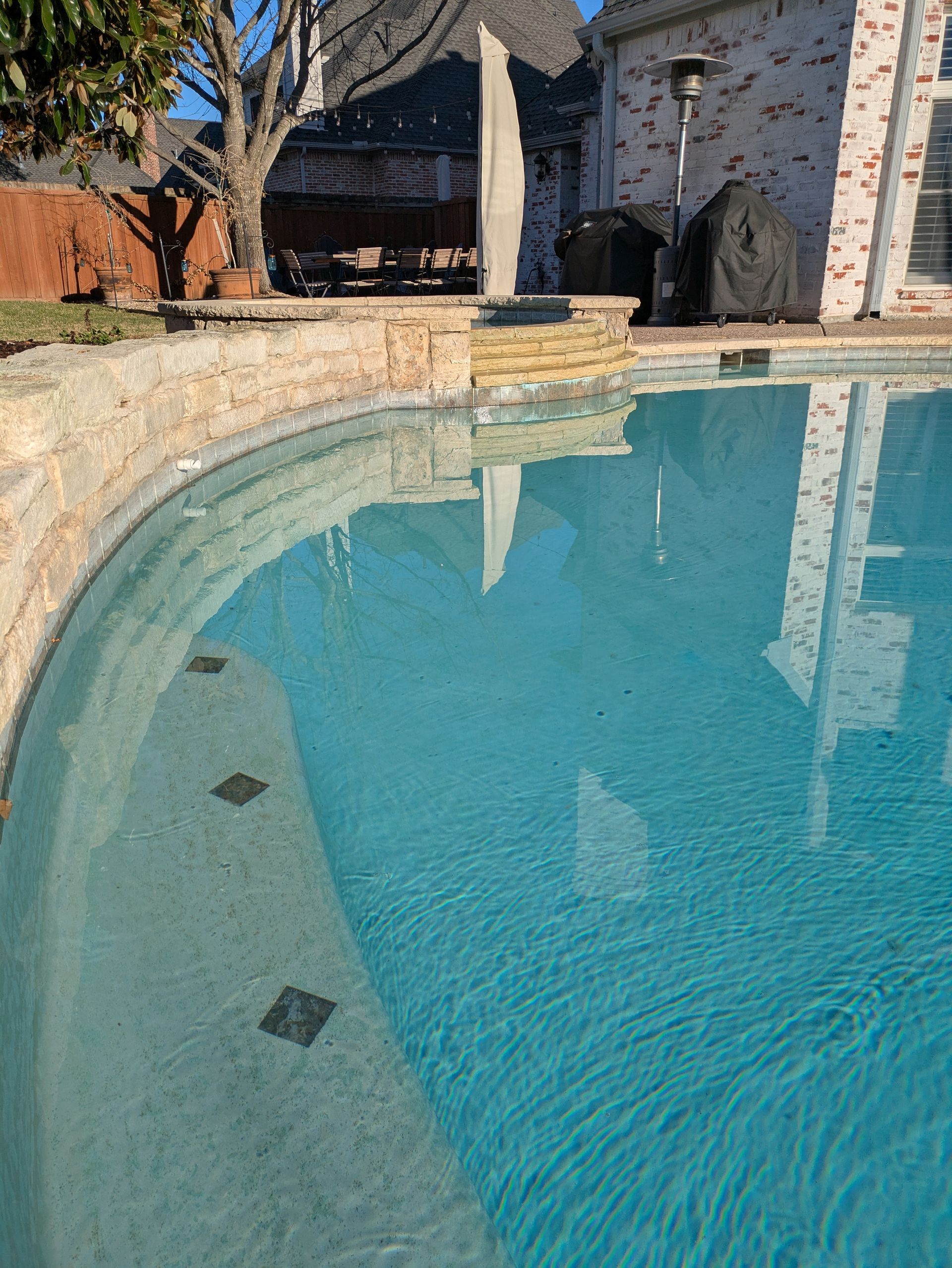 Pool with light blue water, stone coping, and reflection of a structure.