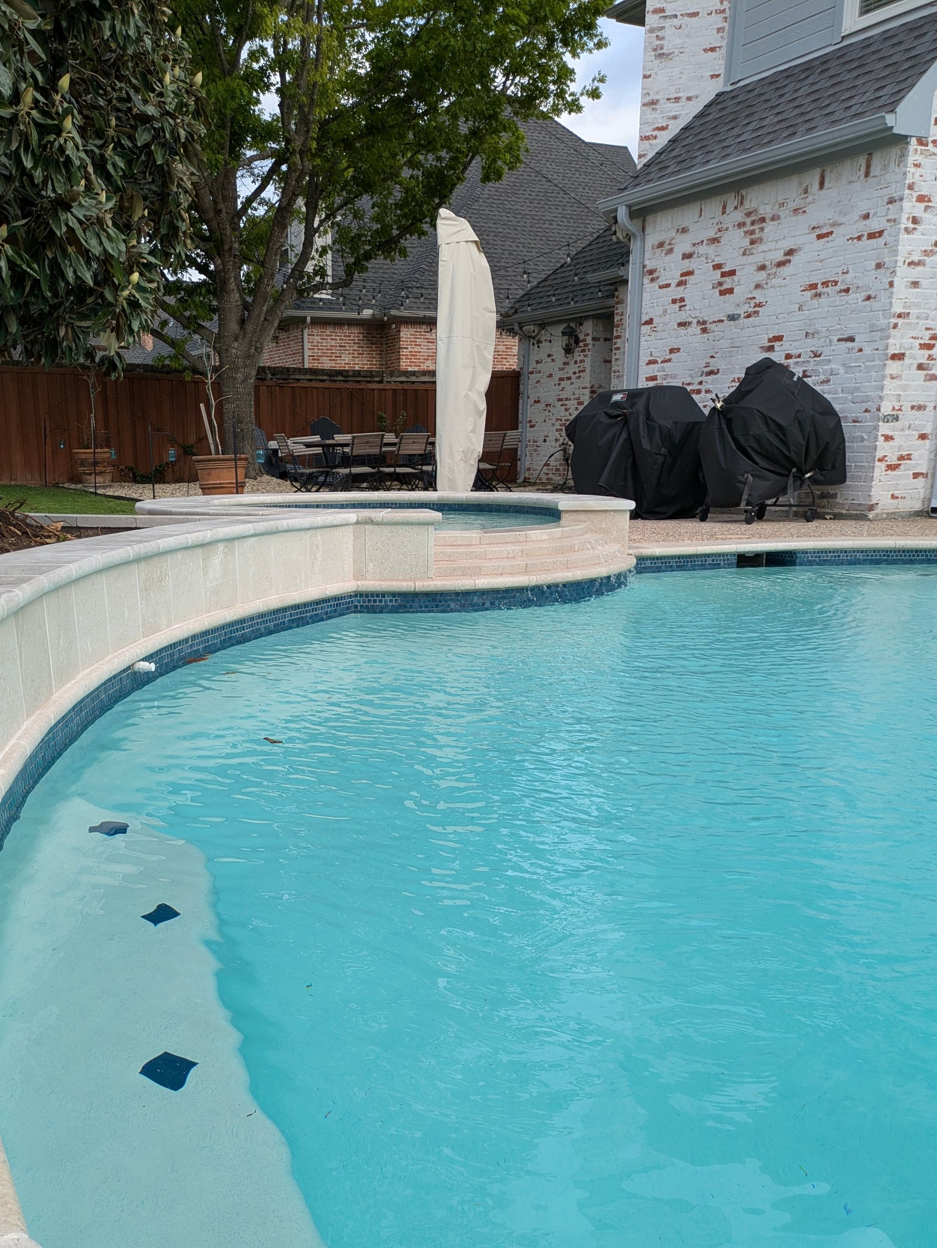 Pool with turquoise water, a raised hot tub, and a brick house.