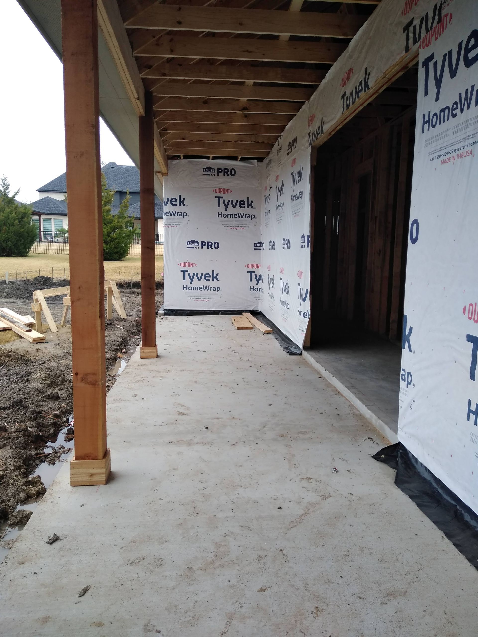A porch under construction, with wooden supports and concrete floor, covered in Tyvek.