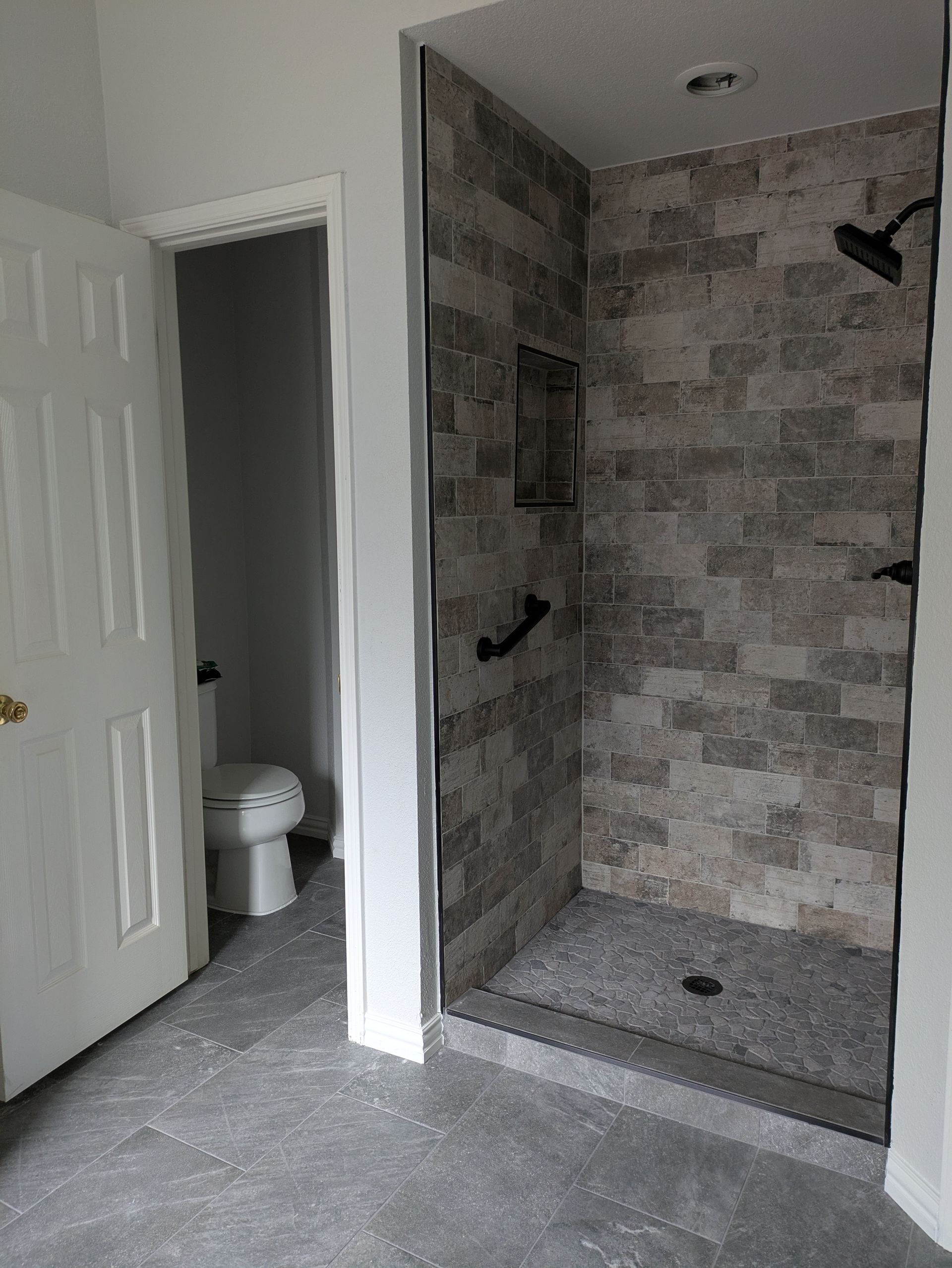 Bathroom with gray tile shower and toilet visible in the doorway.