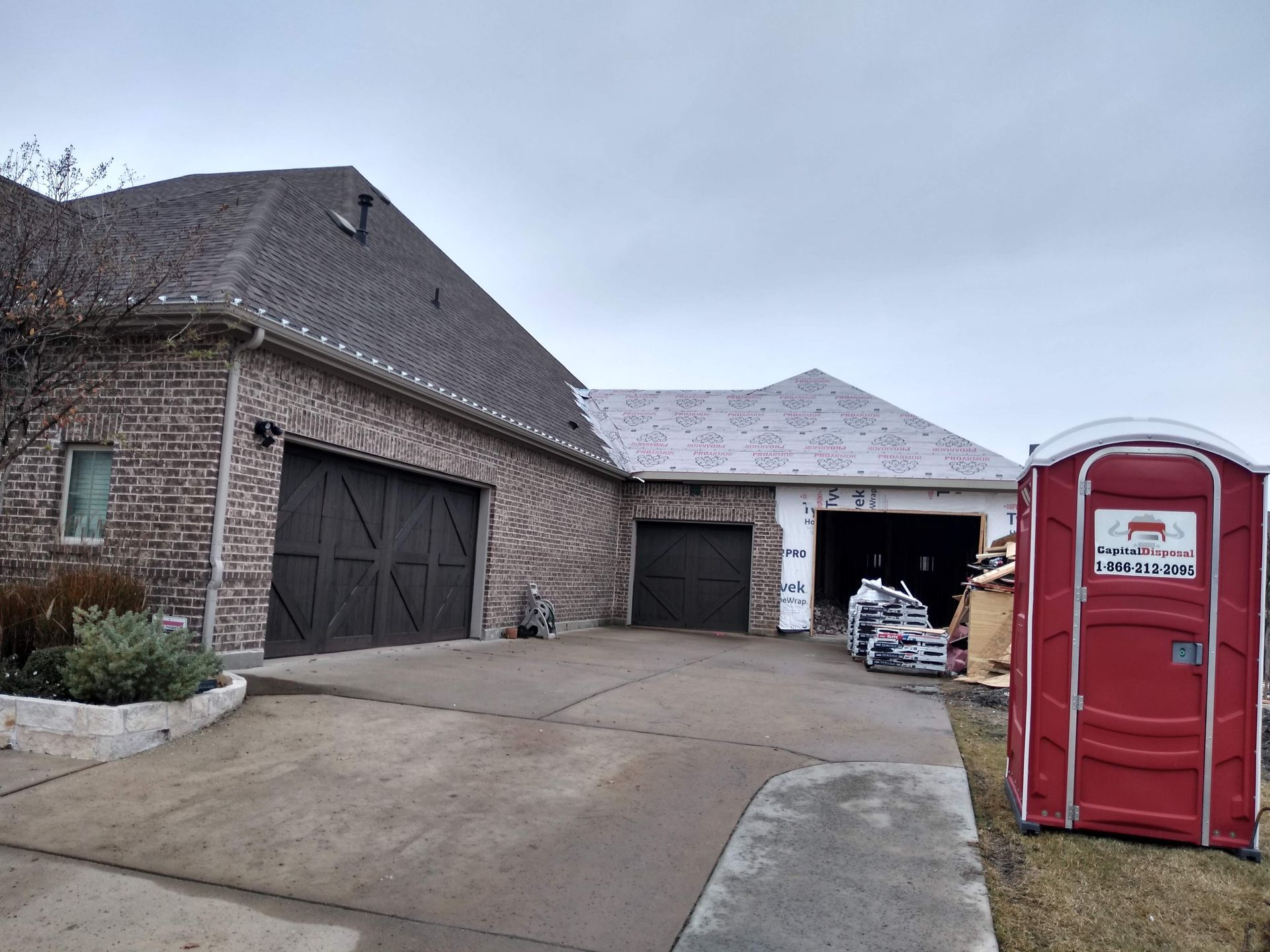 A red portable toilet is in front of a large brick house.