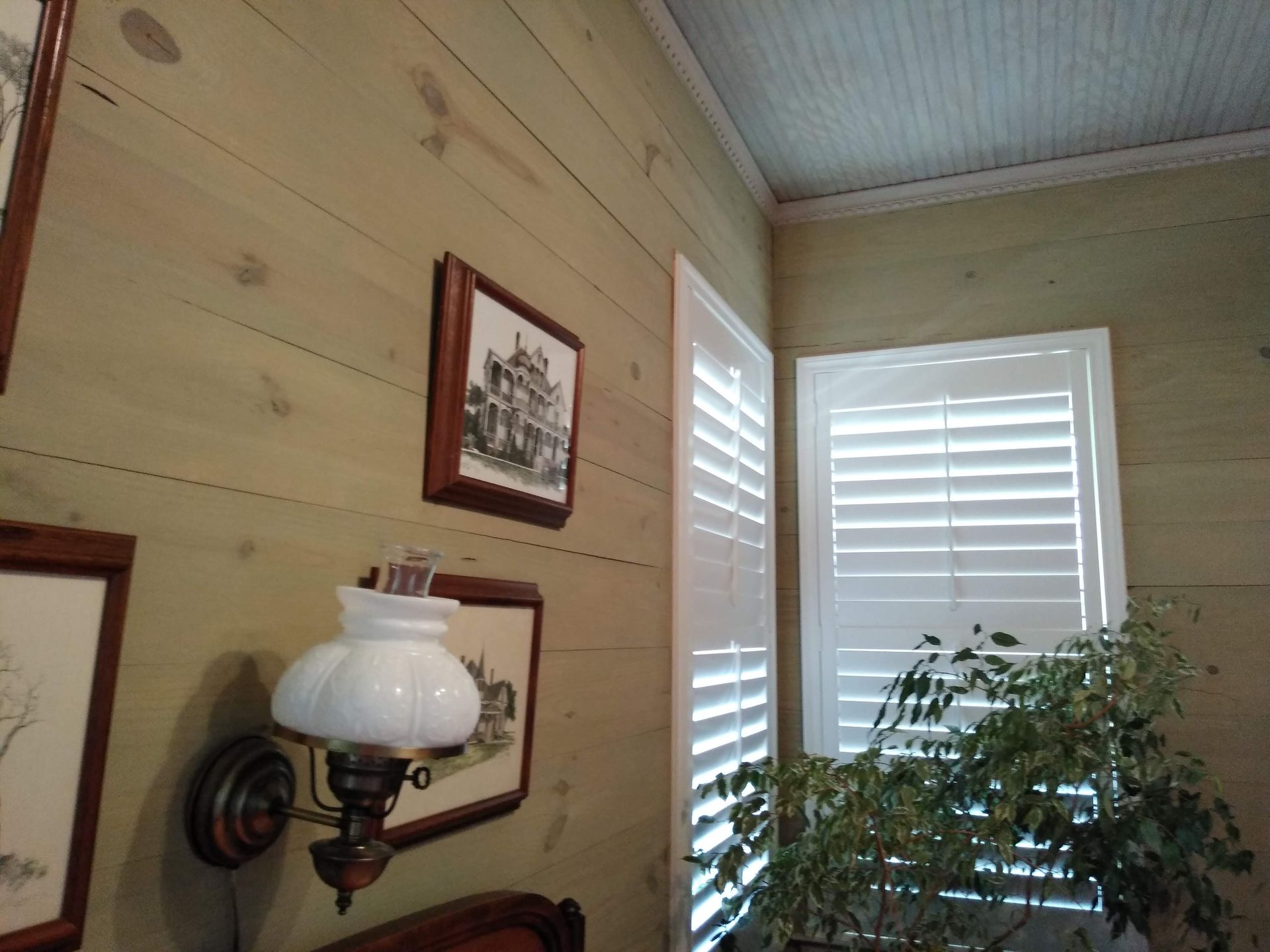 A bedroom with shutters and a lamp on the wall