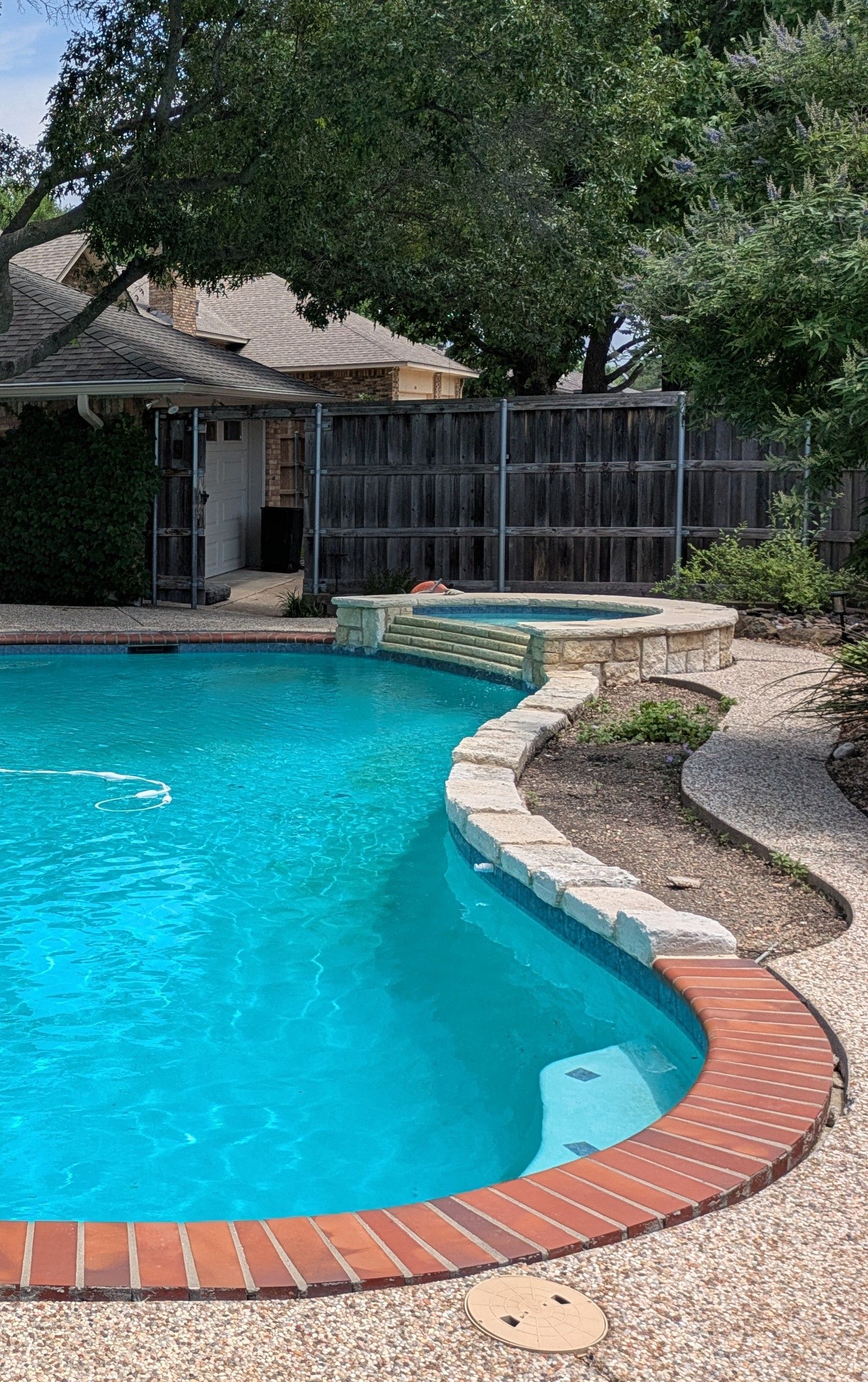 Swimming pool with a turquoise interior, brick edge, and stone pathway leading to a hot tub.