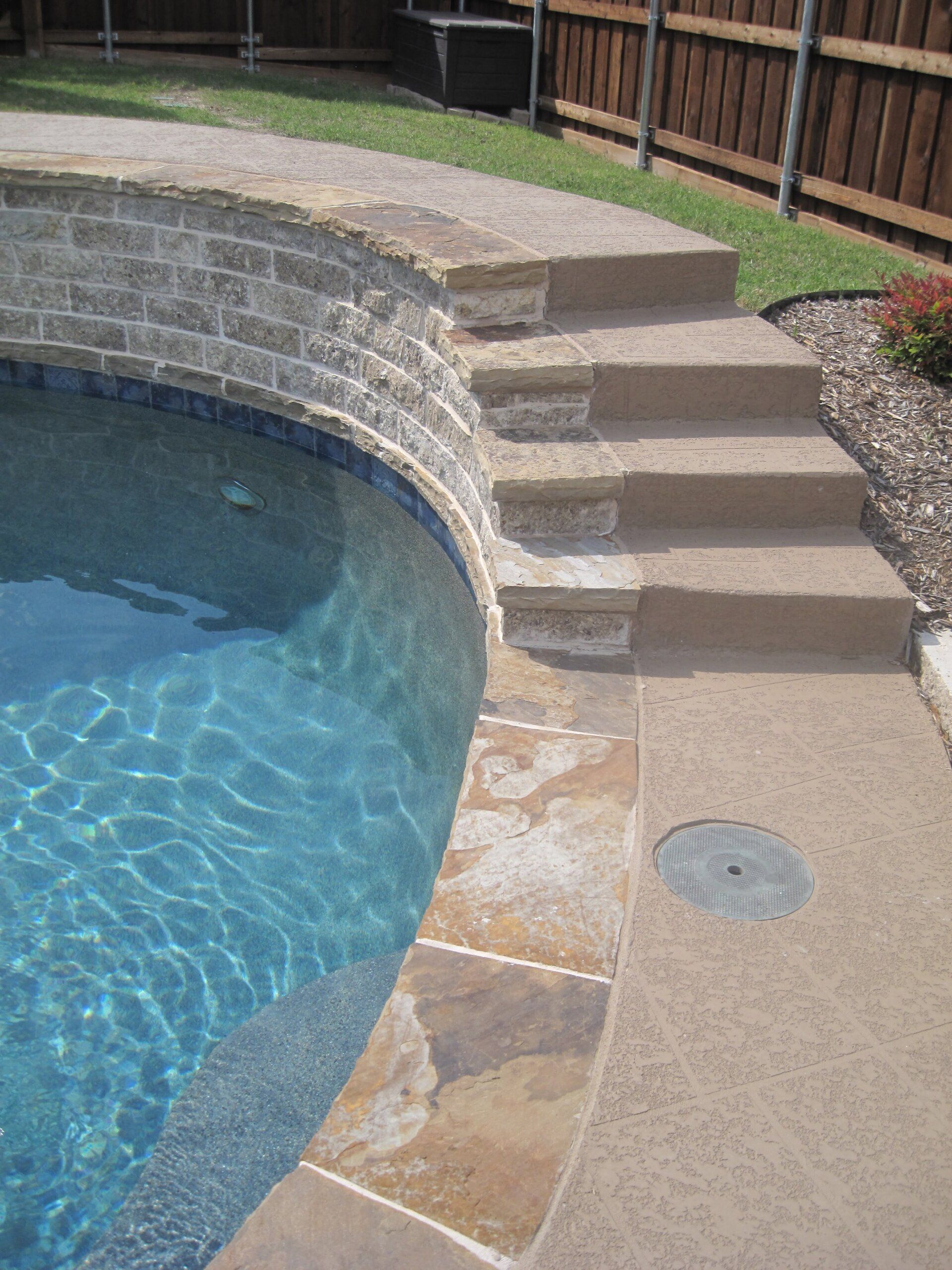 A swimming pool with stairs leading to it and a wooden fence in the background.