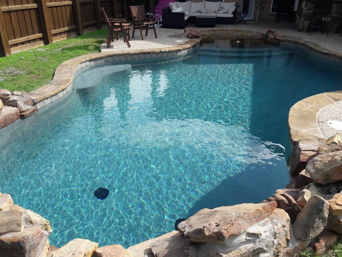 A large swimming pool surrounded by rocks in a backyard