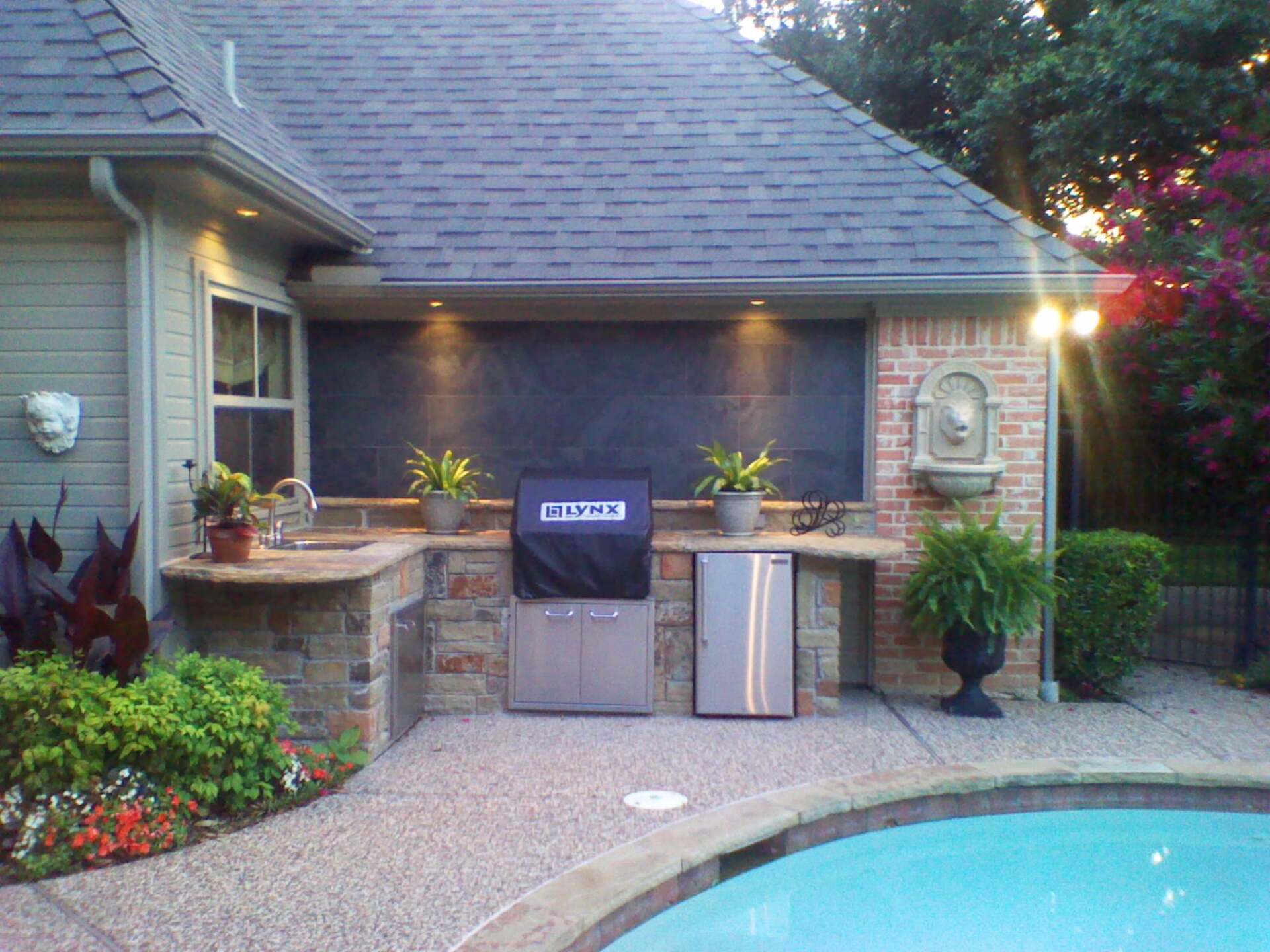 A stainless steel grill with a black cover is sitting next to a swimming pool