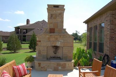 A large stone fireplace is in the backyard of a brick house