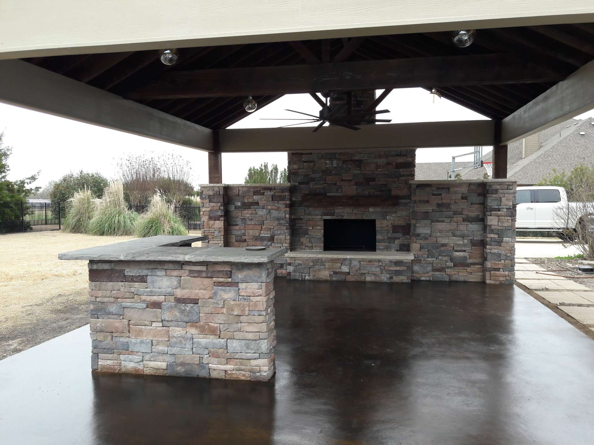 A patio with a stone fireplace and a ceiling fan