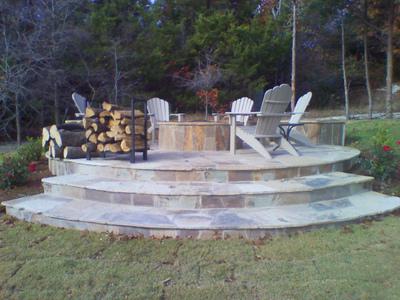 A stone patio with chairs and a fire pit in the backyard.