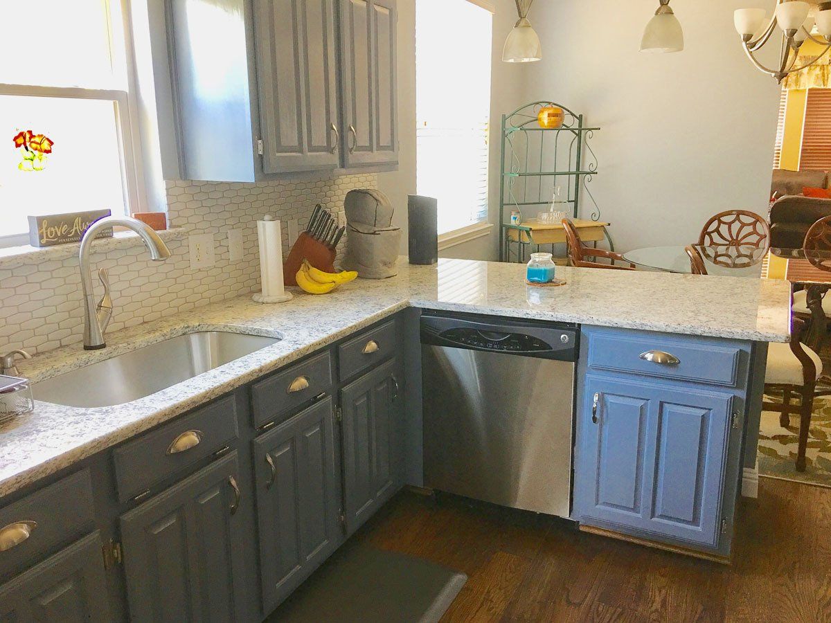 A kitchen with gray cabinets , a sink , and a stainless steel dishwasher.