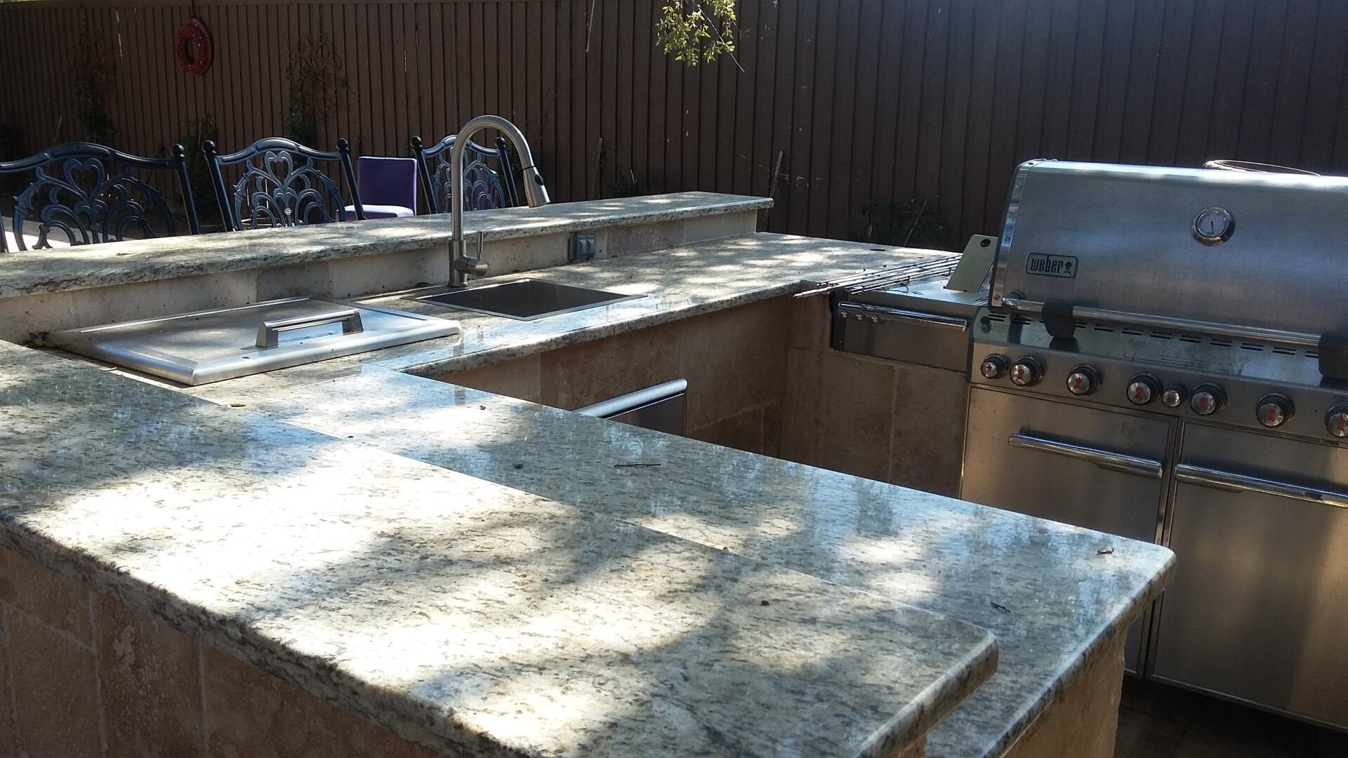 An outdoor kitchen with granite counter tops and a grill