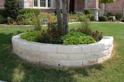 A brick wall with flowers and a tree in it in front of a house.