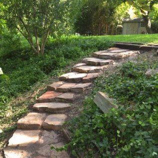 A stone walkway in a garden with a shed in the background.