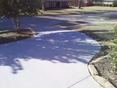 A concrete driveway leading to a house with trees in the background