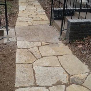 A stone walkway leading to a house with stairs.