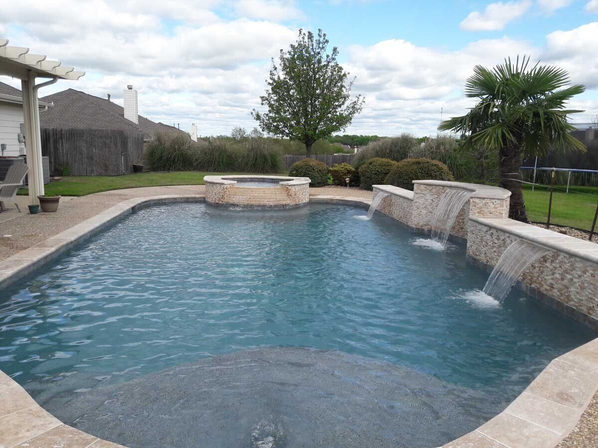 A large swimming pool with a waterfall in the backyard.
