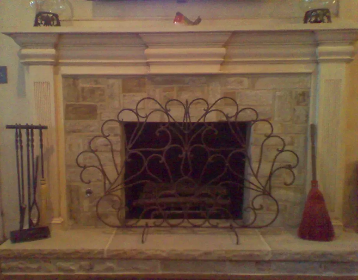 A fireplace with a wrought iron fireplace screen and a broom on the mantle.