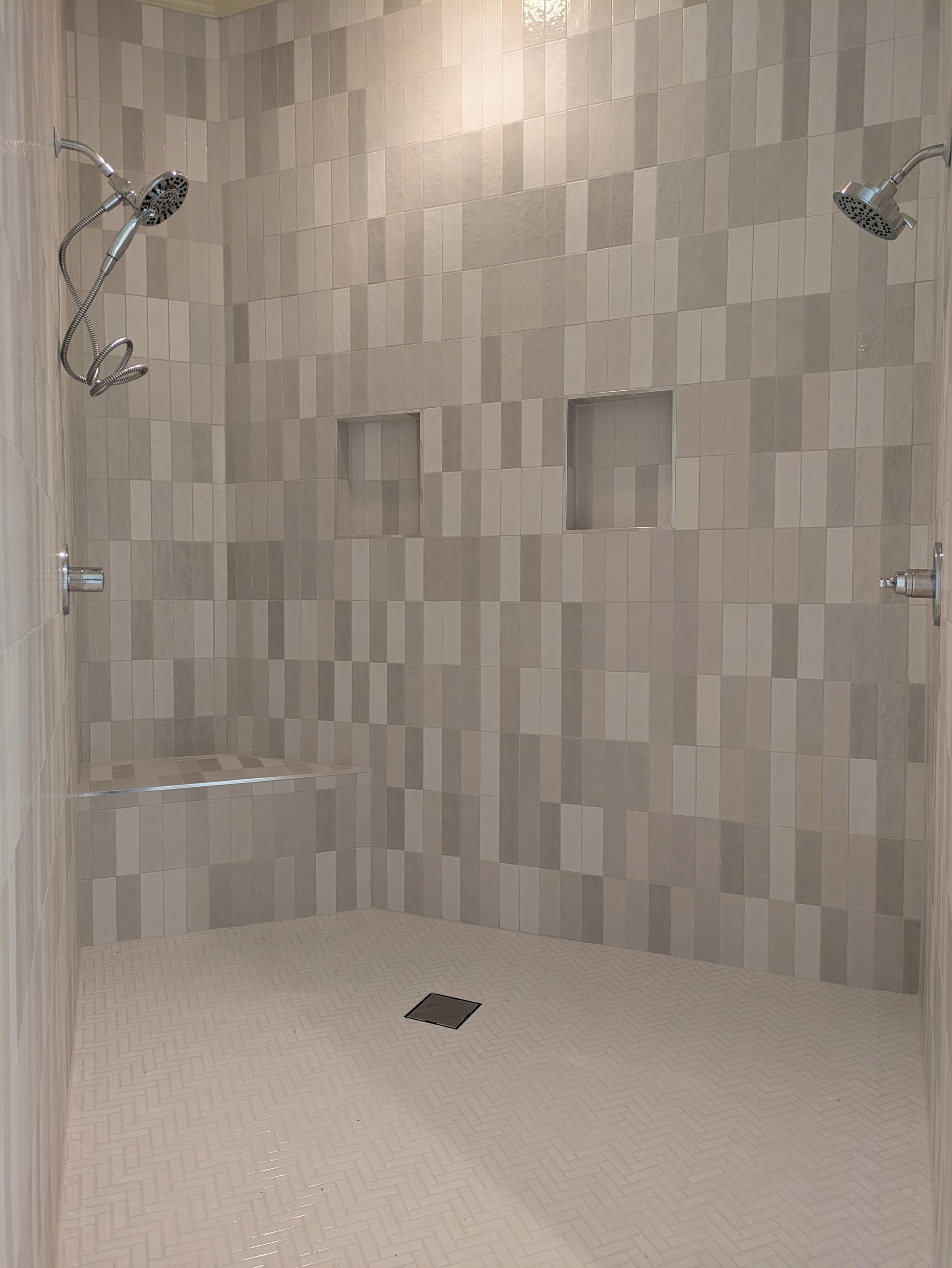 A tiled shower with two shower heads, a built-in bench, and two recessed shelves.