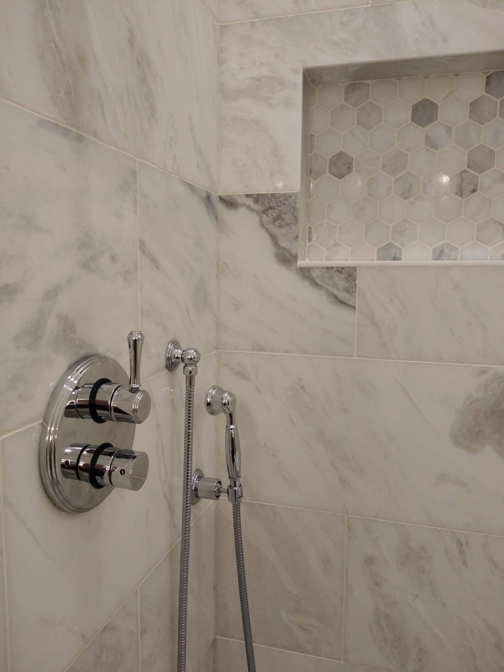 A bathroom with marble tiles and a shower head.
