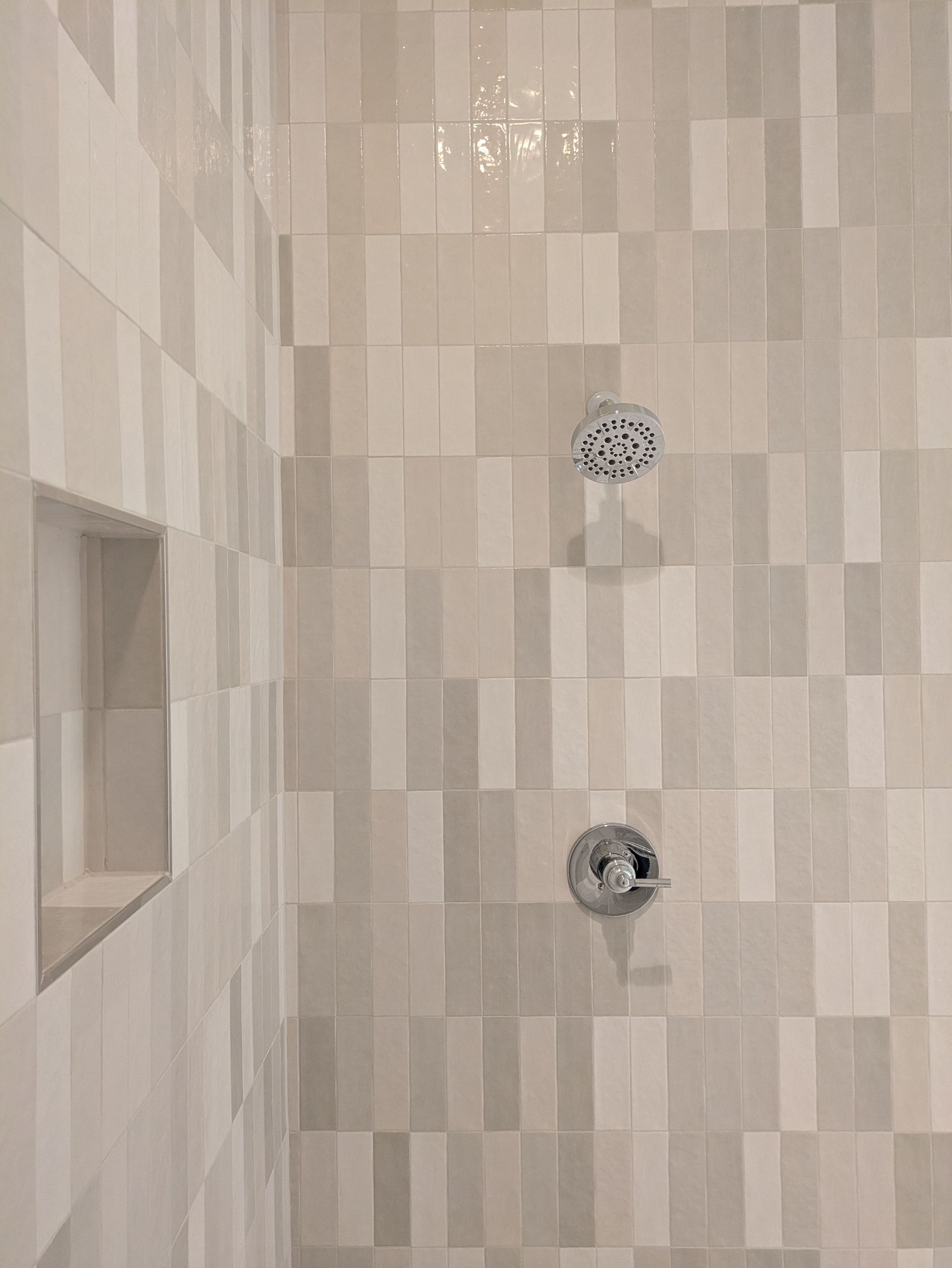 Shower with off-white rectangular tiles in a staggered pattern, built-in shelf, and two chrome showerheads.