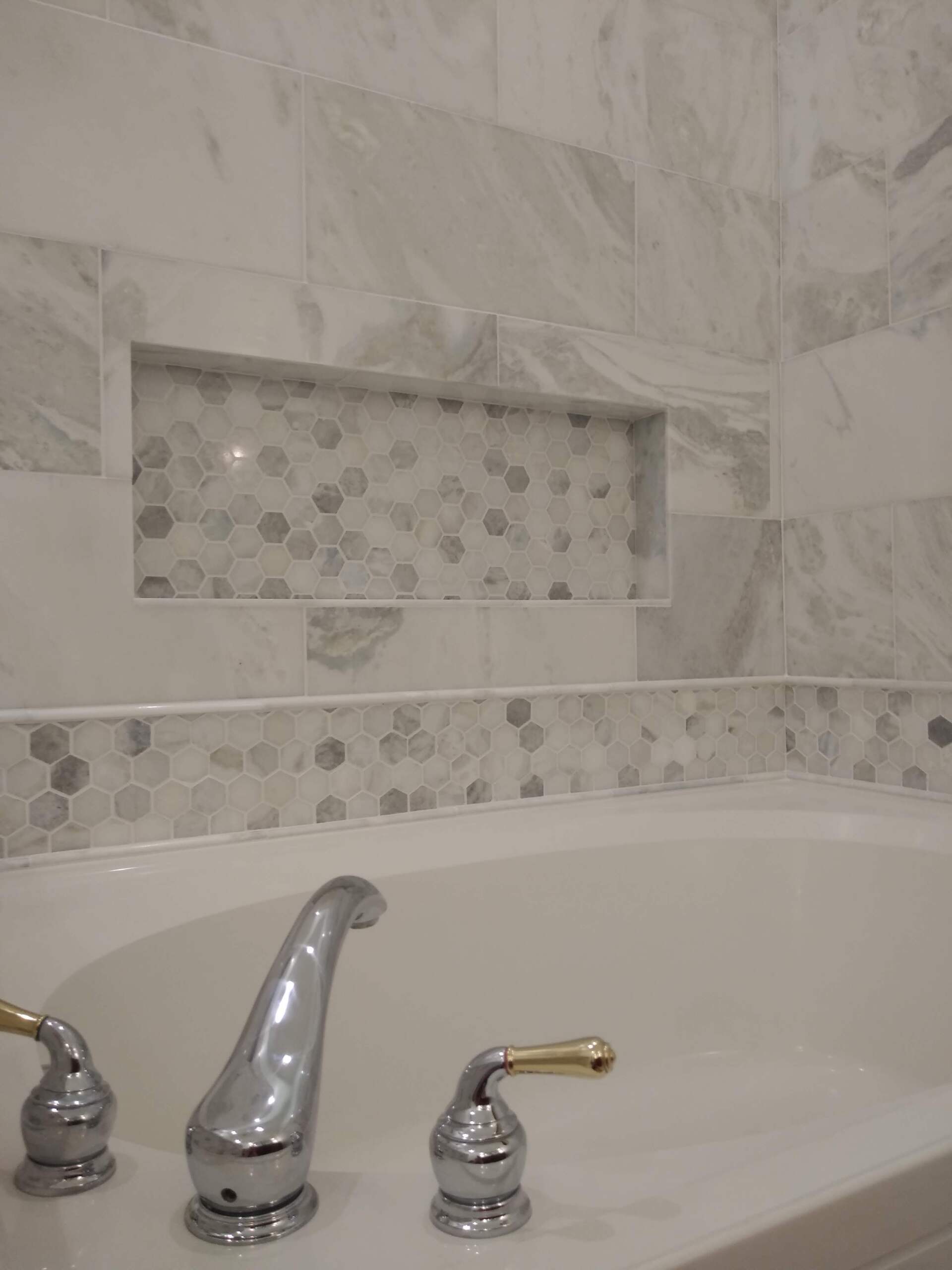 A bathtub with a faucet and a marble wall in a bathroom.