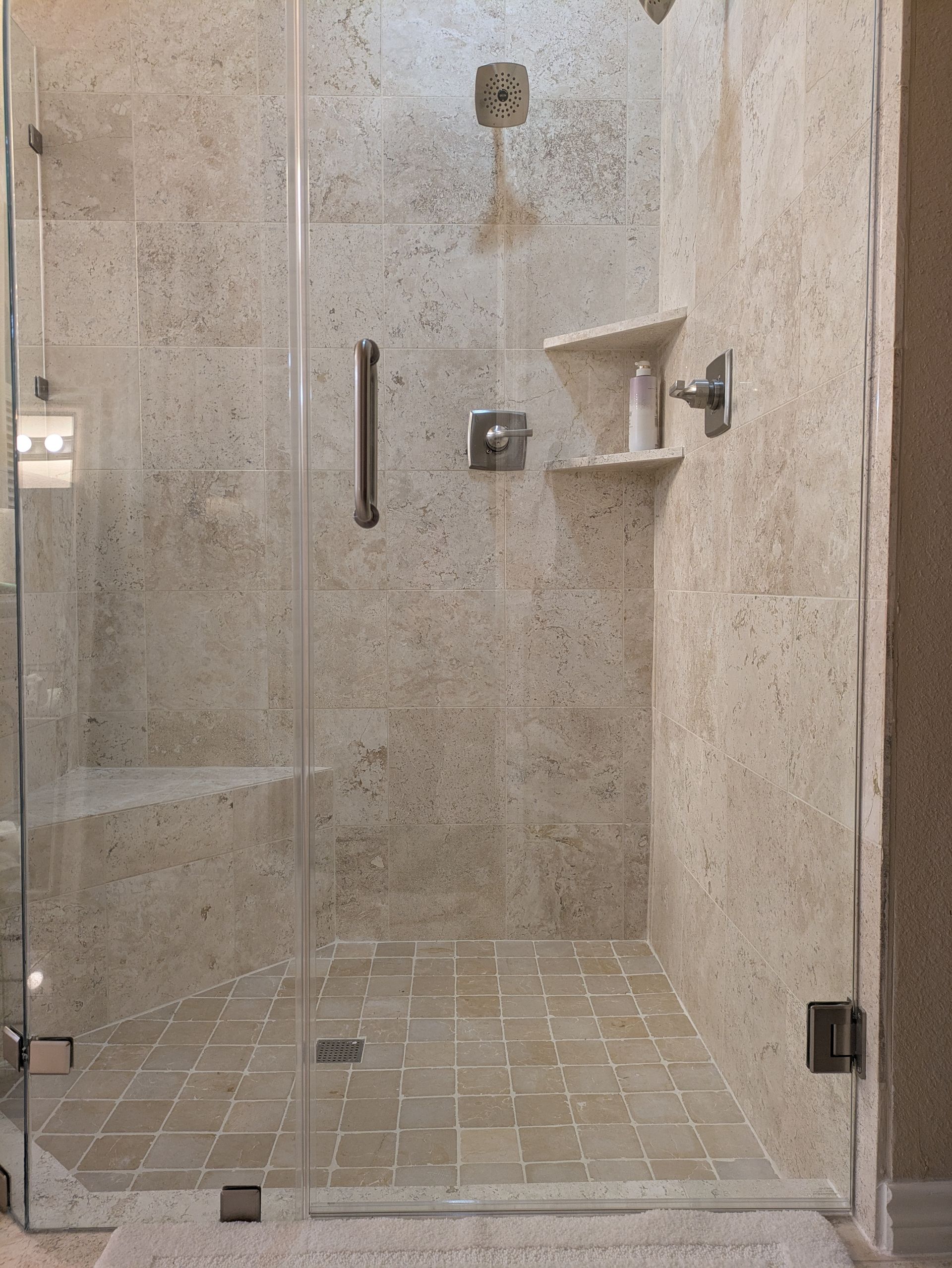 Shower with beige stone tile, clear glass door, and built-in shelves.