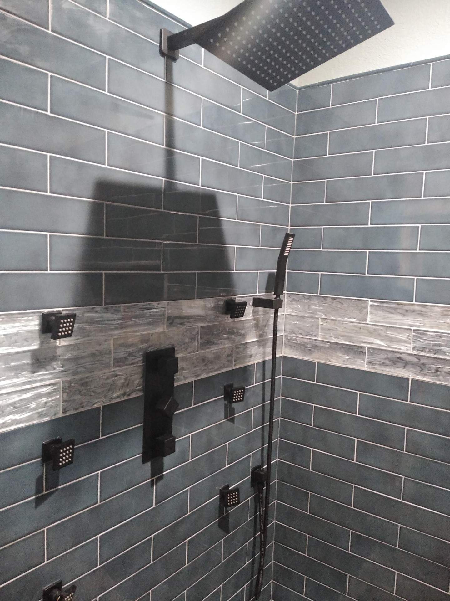 A shower with blue tiles and a black shower head.