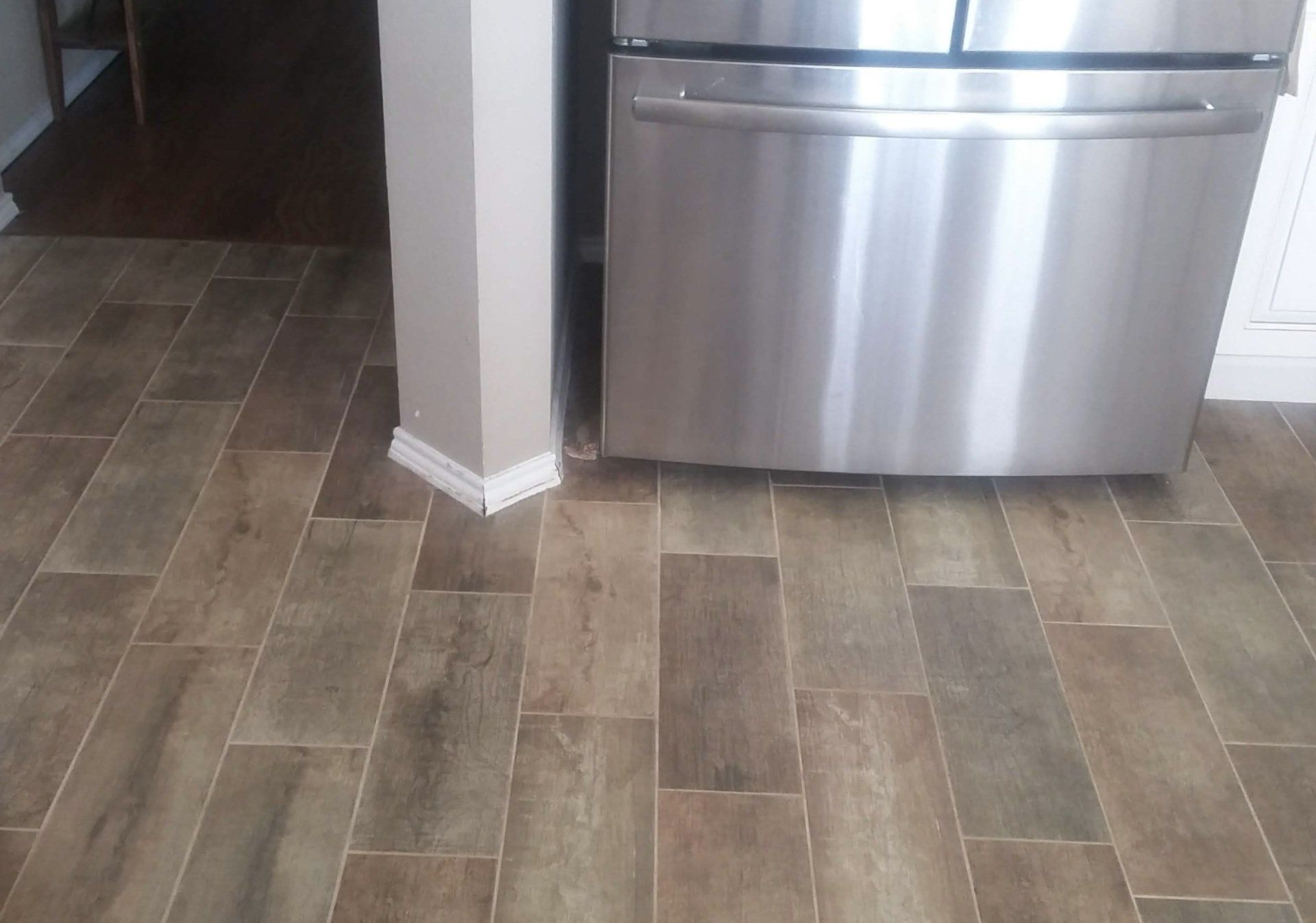 A stainless steel refrigerator is sitting on a wooden floor in a kitchen.