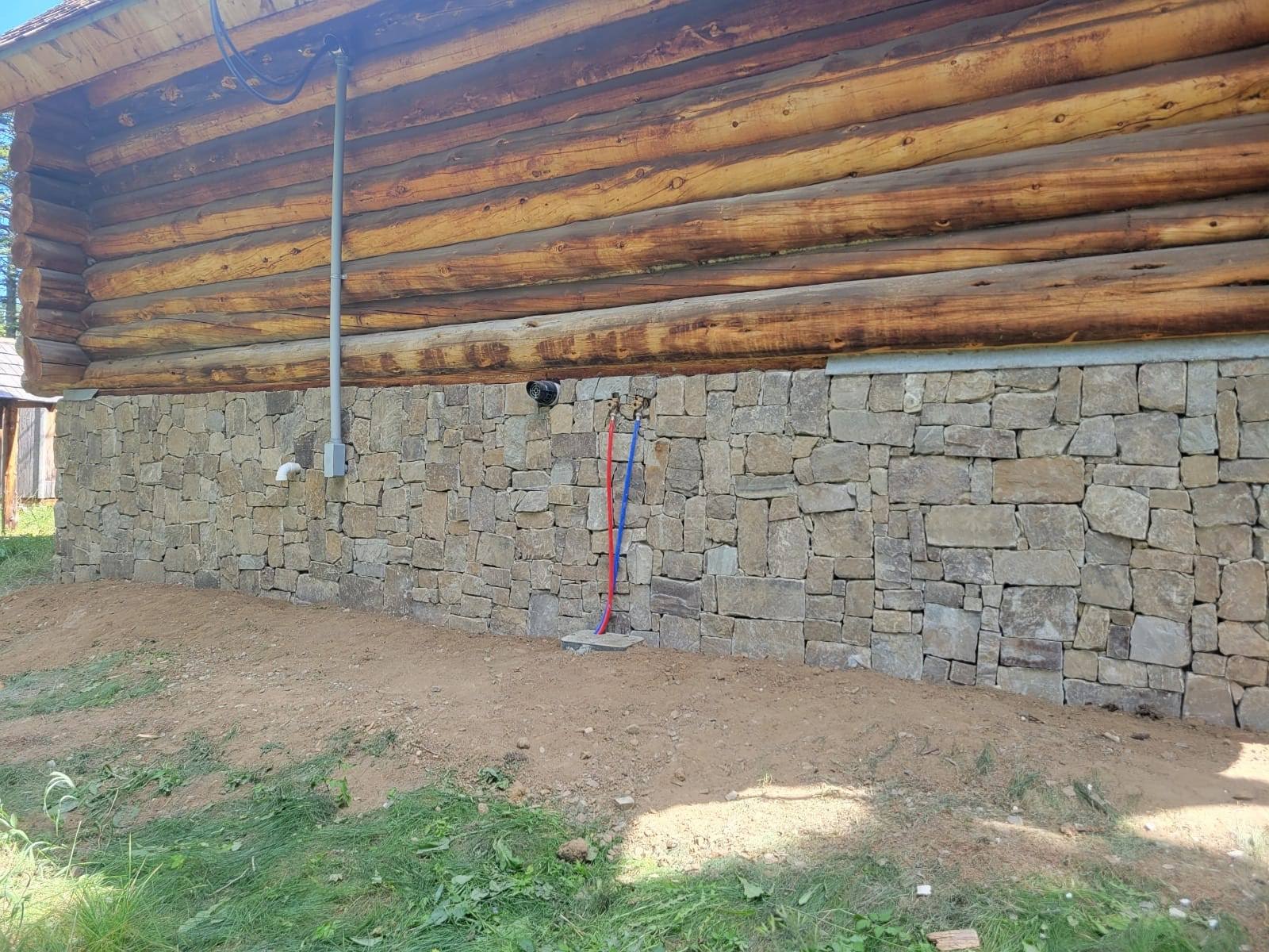 A log cabin with a stone wall on the side of it.