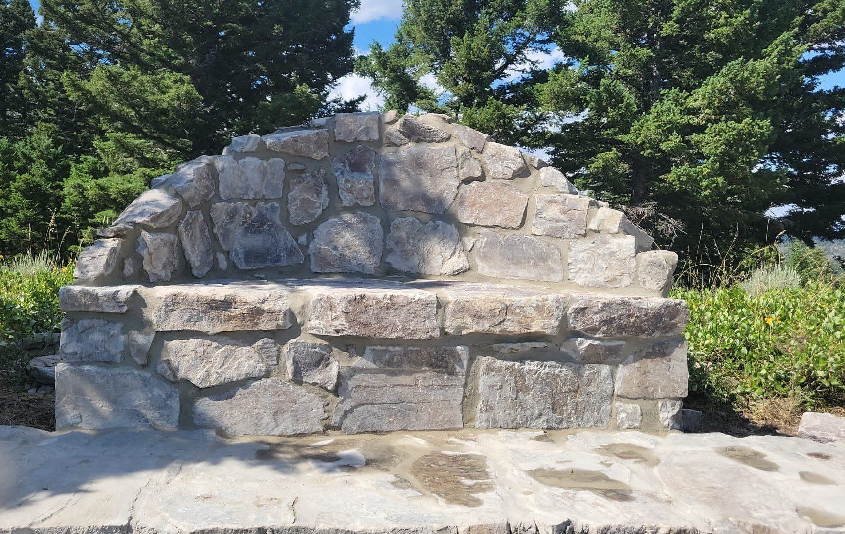 A stone bench in a park with trees in the background