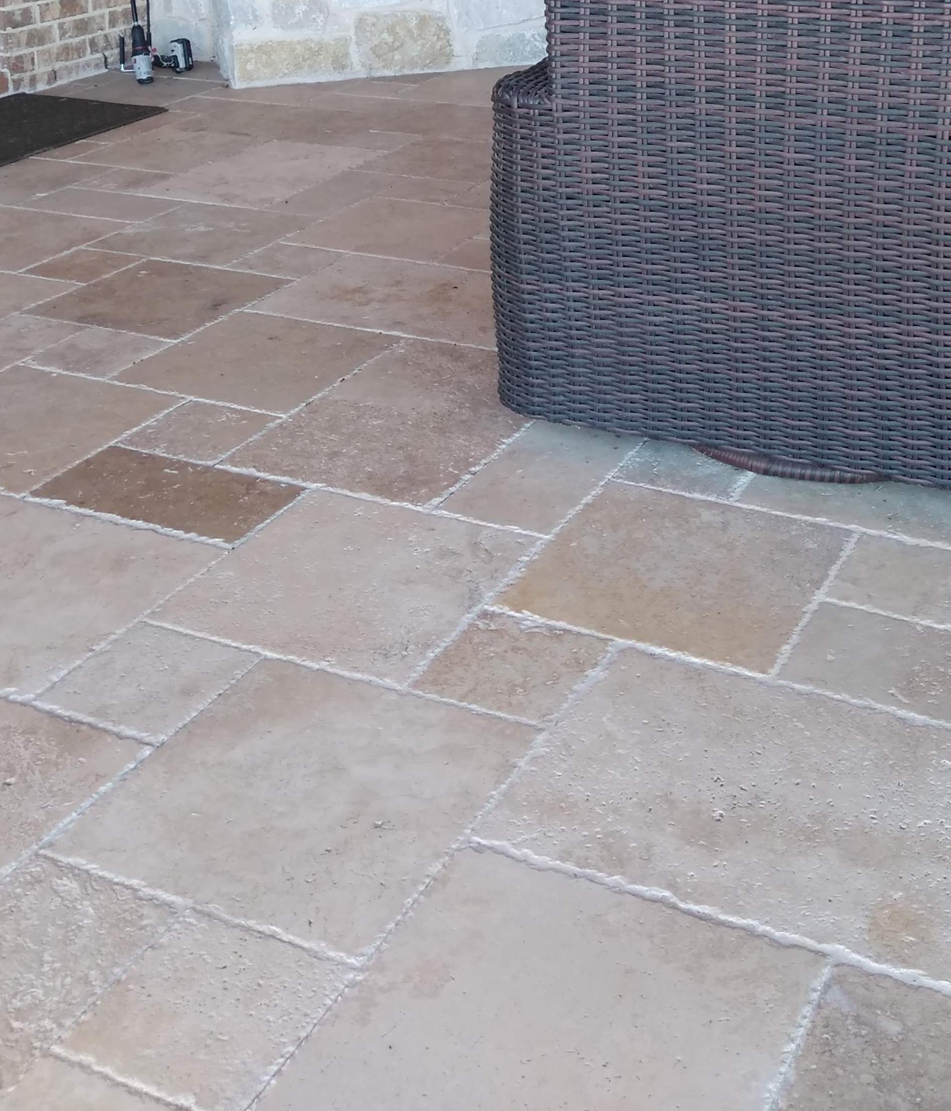 A wicker chair is sitting on a tiled floor next to a brick wall.