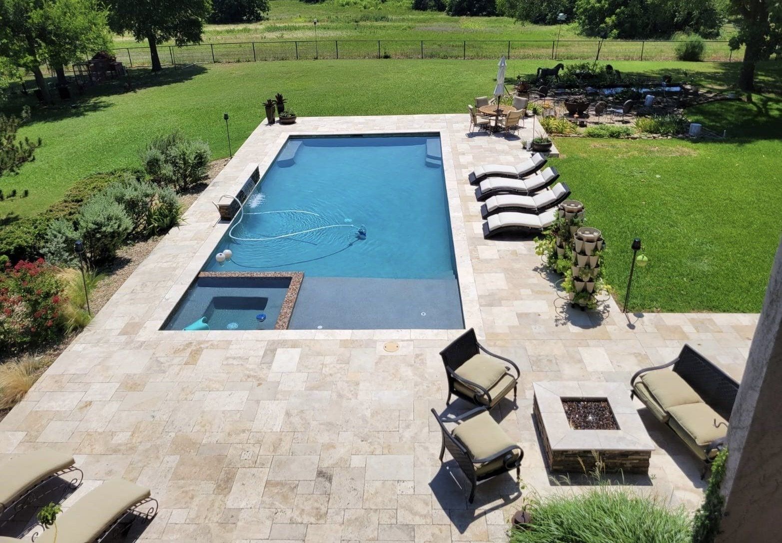 A large swimming pool is surrounded by lawn chairs and a fire pit