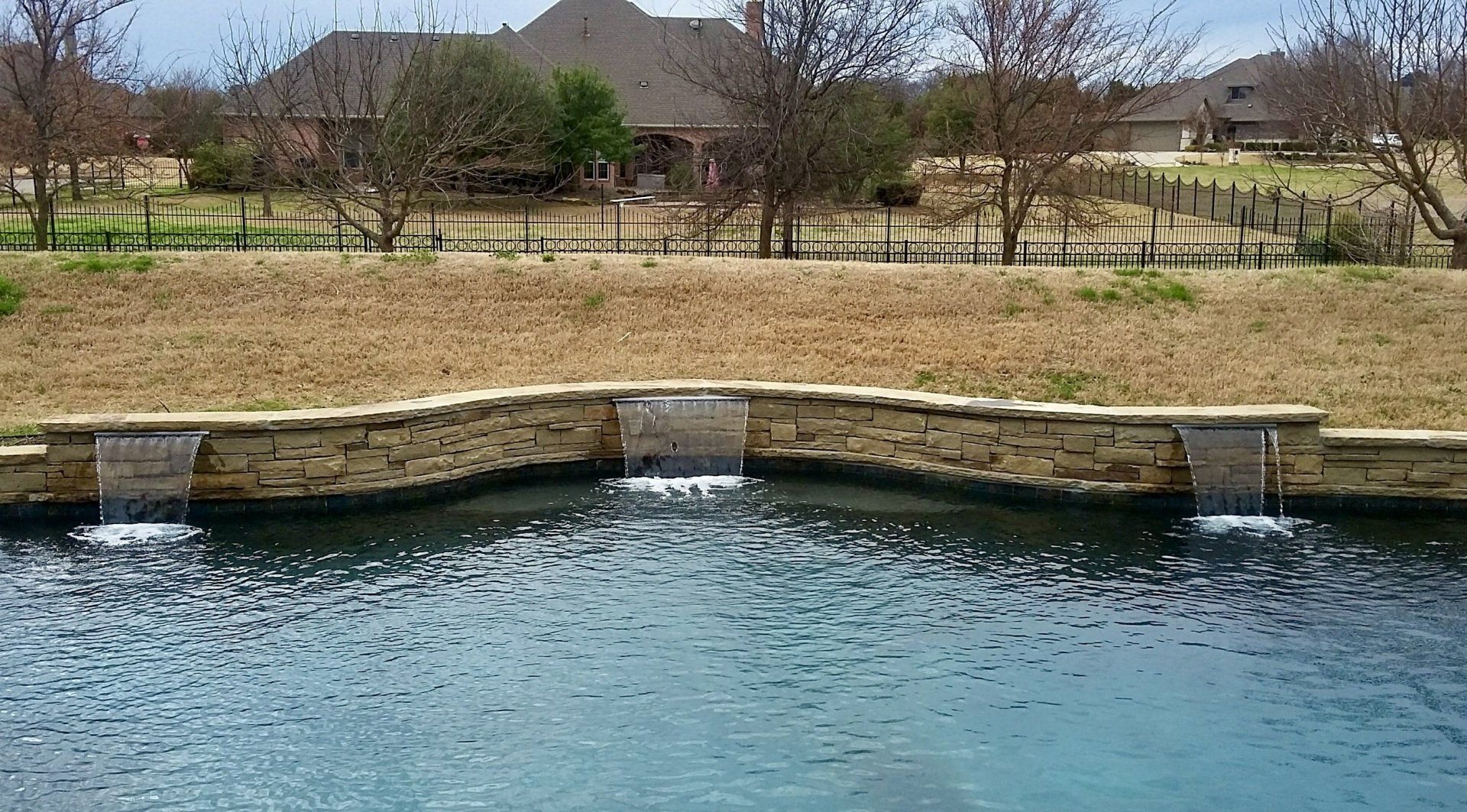 A stone wall surrounds a pond with a house in the background
