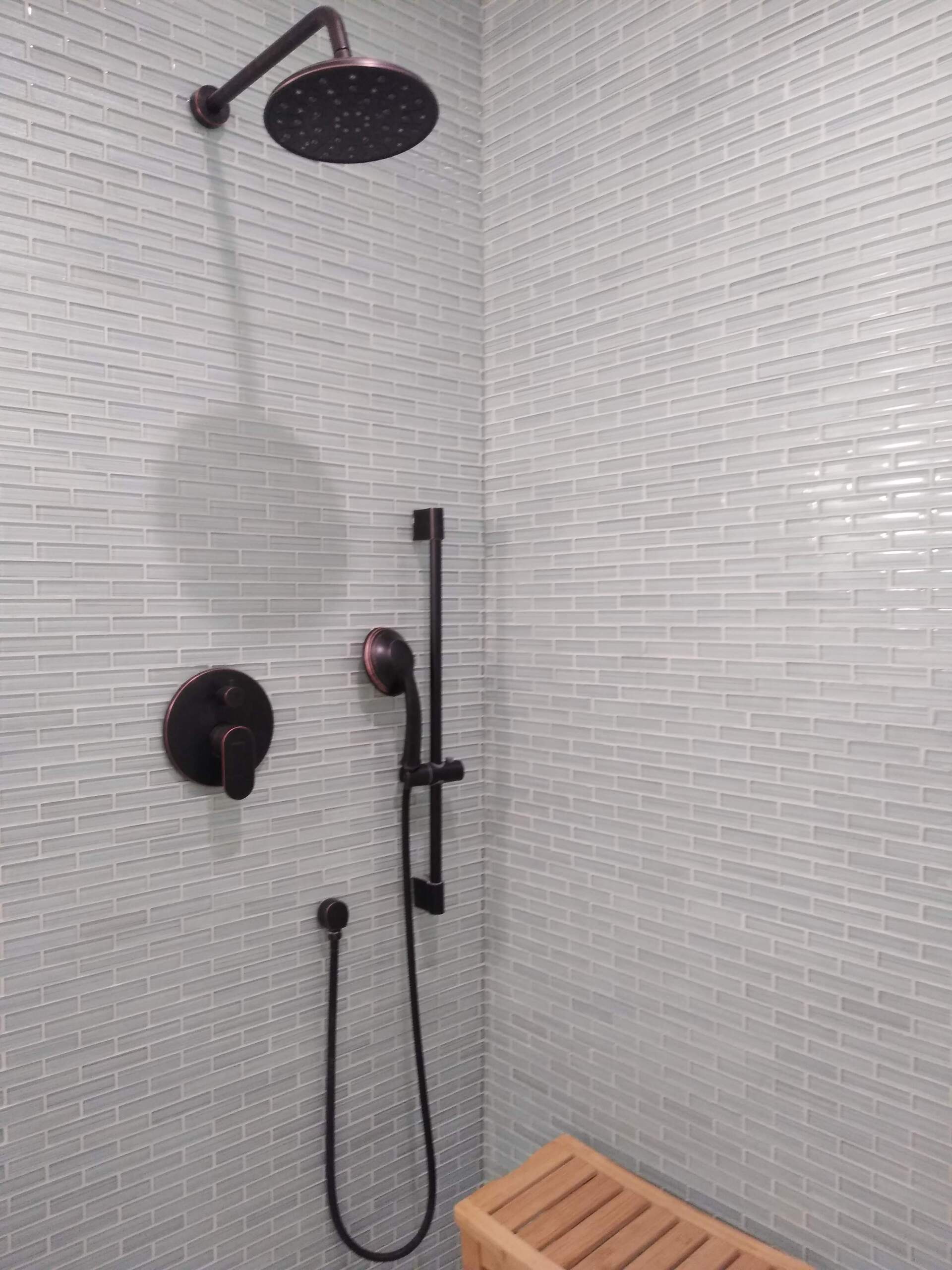 A shower with a black shower head and a wooden bench.