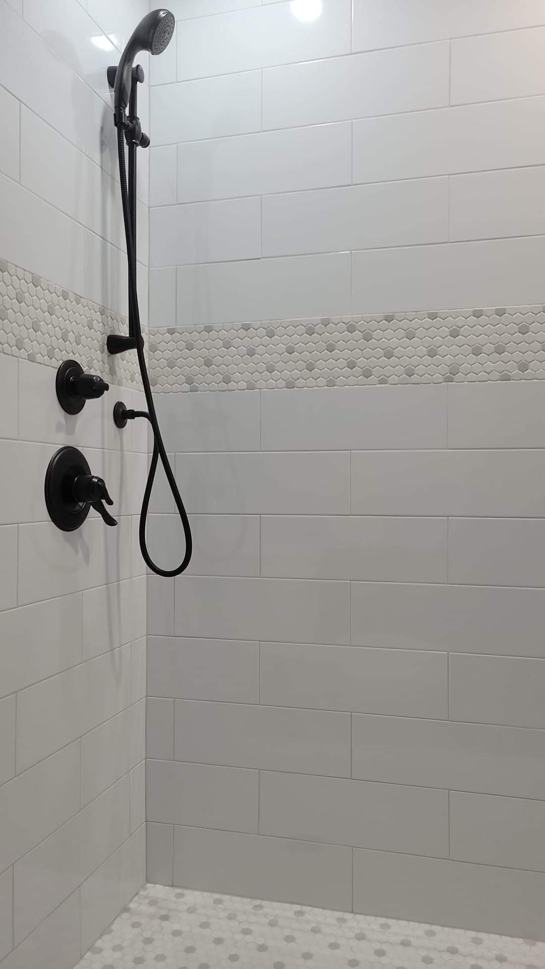 A shower with white tiles and a black shower head.