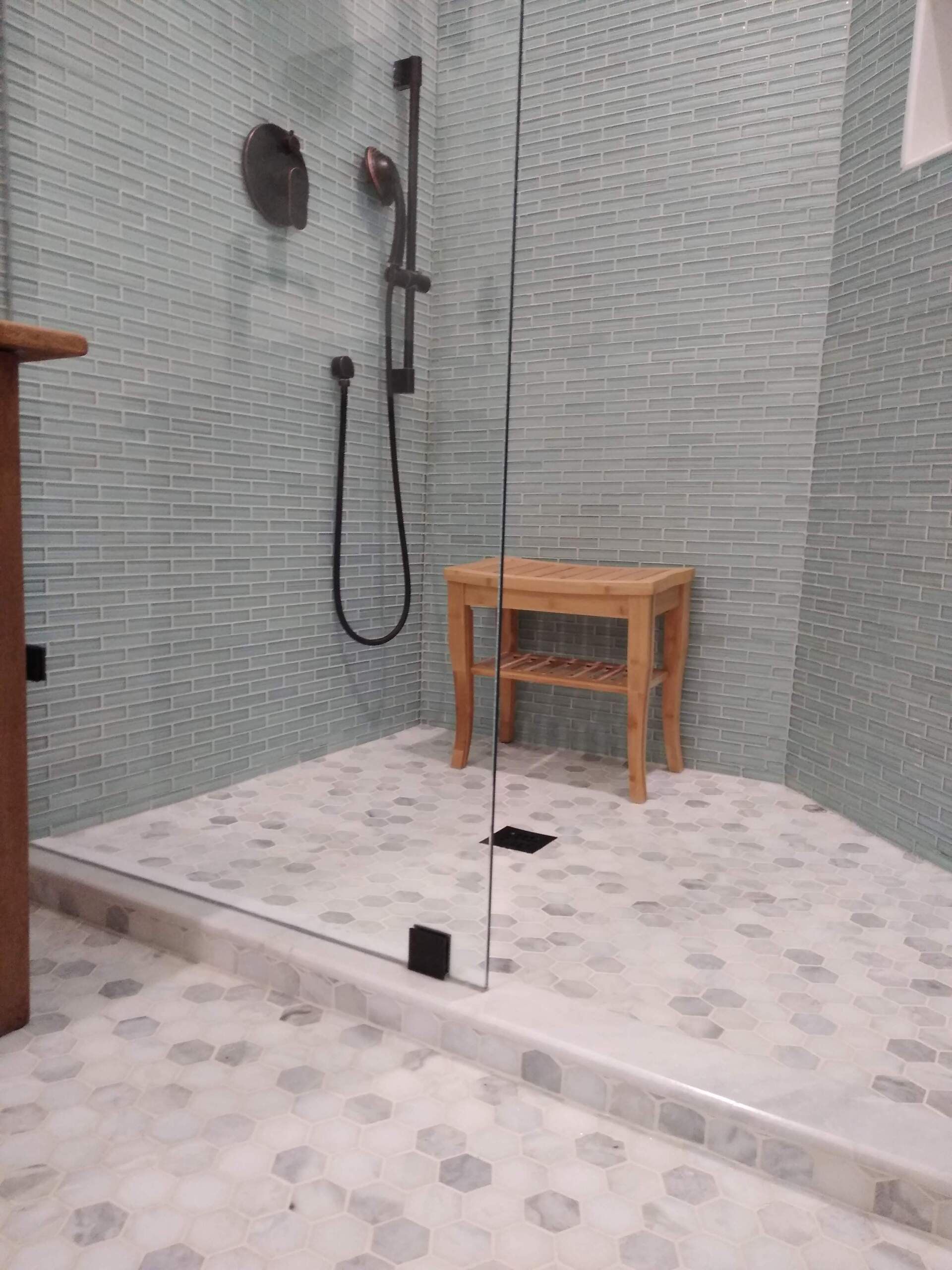 A bathroom with a walk in shower and a wooden bench.