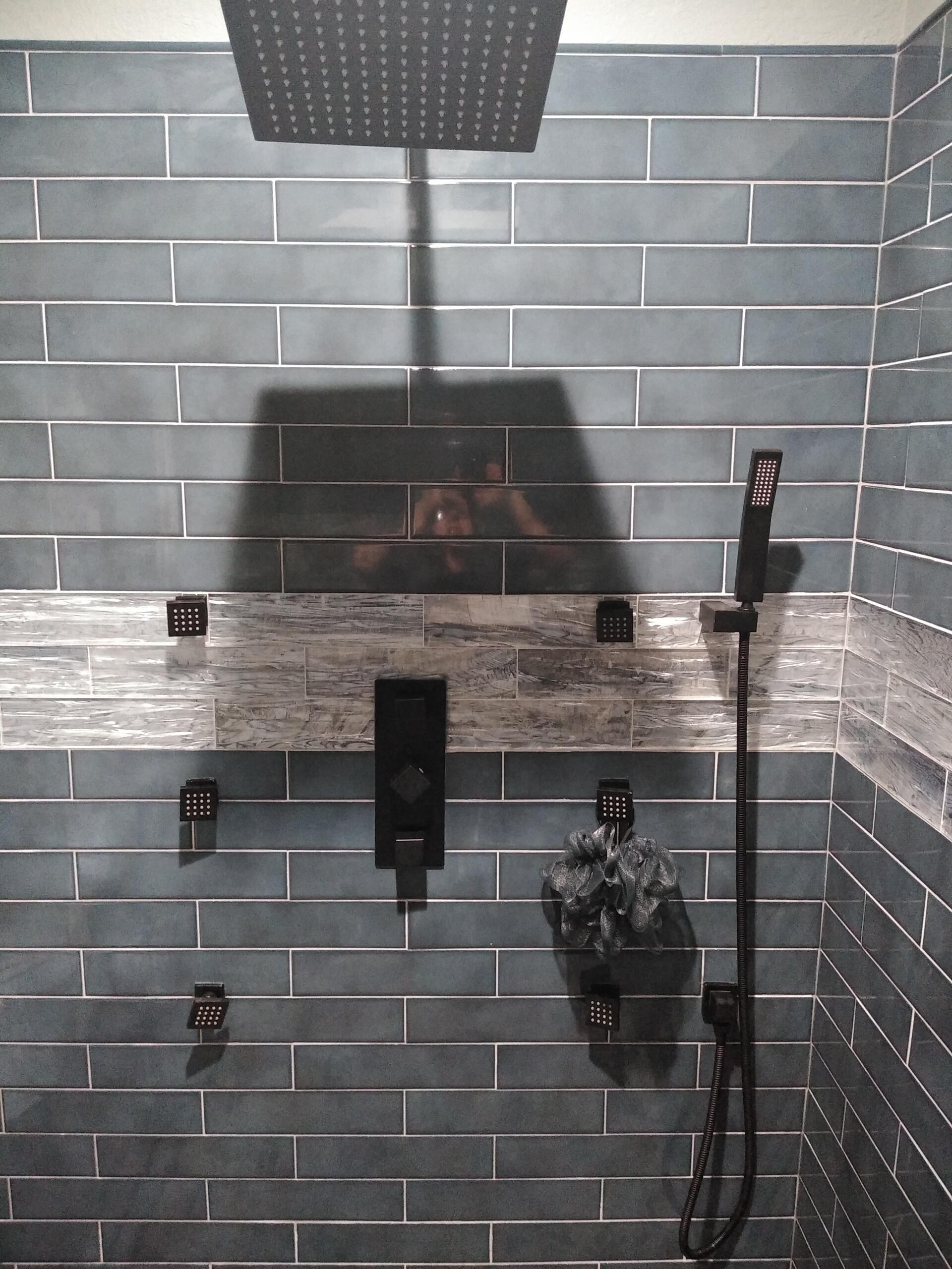 A shower with blue tiles and a black shower head