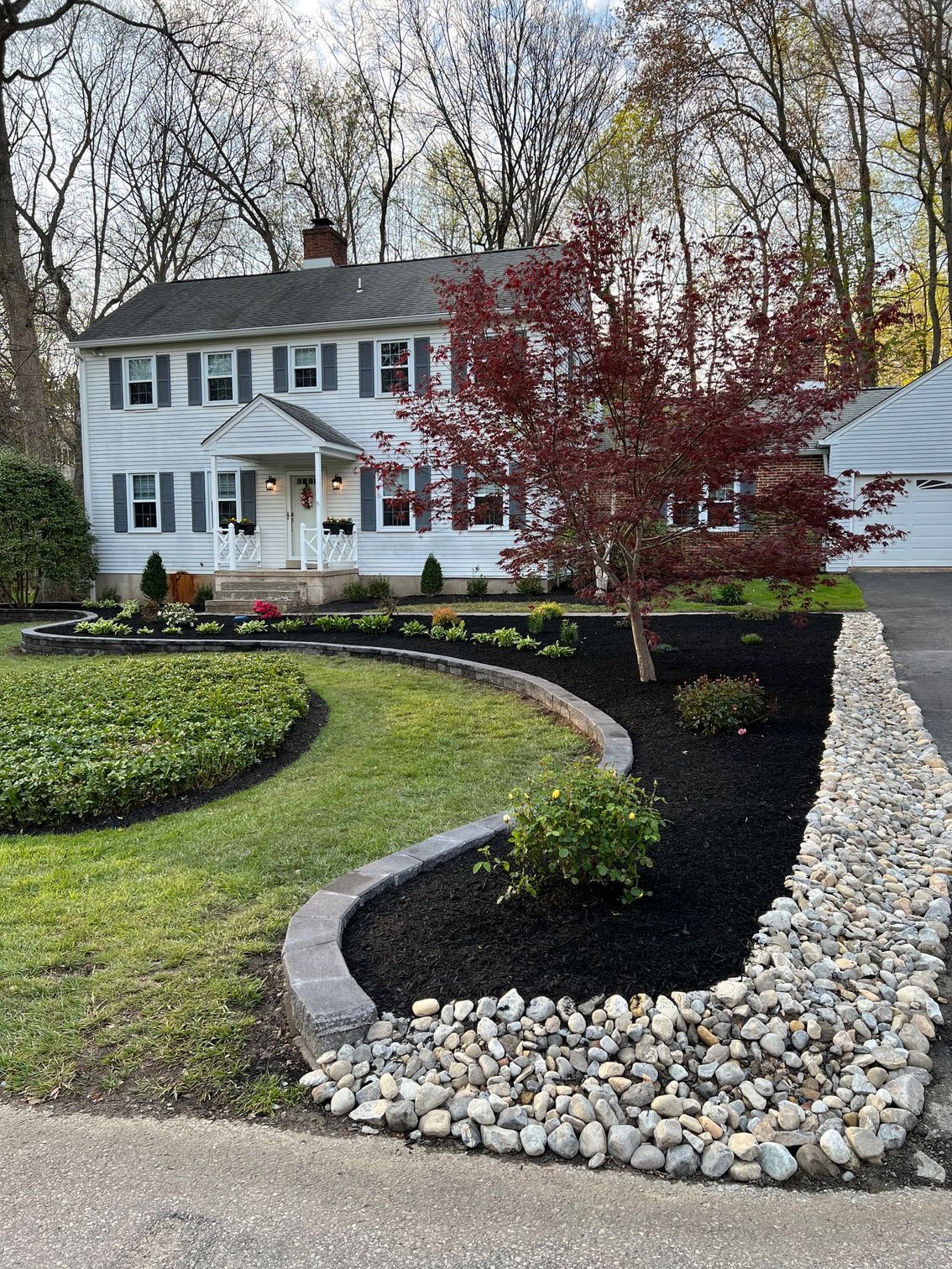 A large white house with a lush green lawn and a rock wall in front of it.